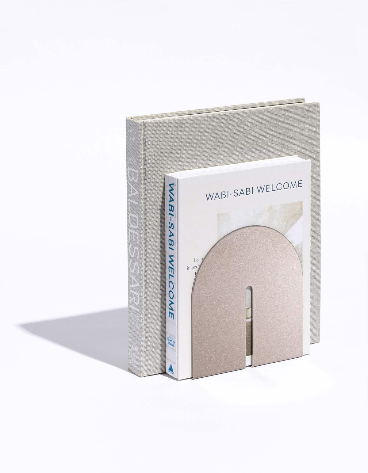 Pale taupe bookend from Tortuga Forma Dumbo Bookend Pairs - The Architect Collection holding two upright books on white, with its curved panel covering the lower portion of the front book.