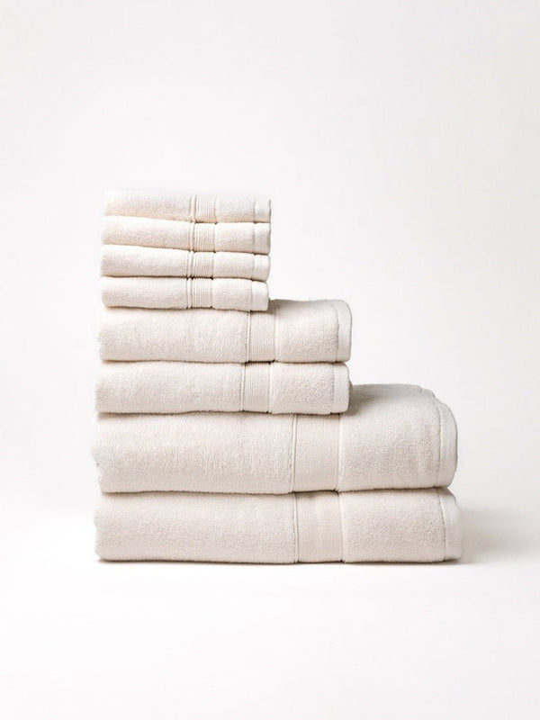 Ivory towel set stacked by size on a pale background, with four washcloths above two hand towels and two bath towels, showing plush texture and woven border bands.