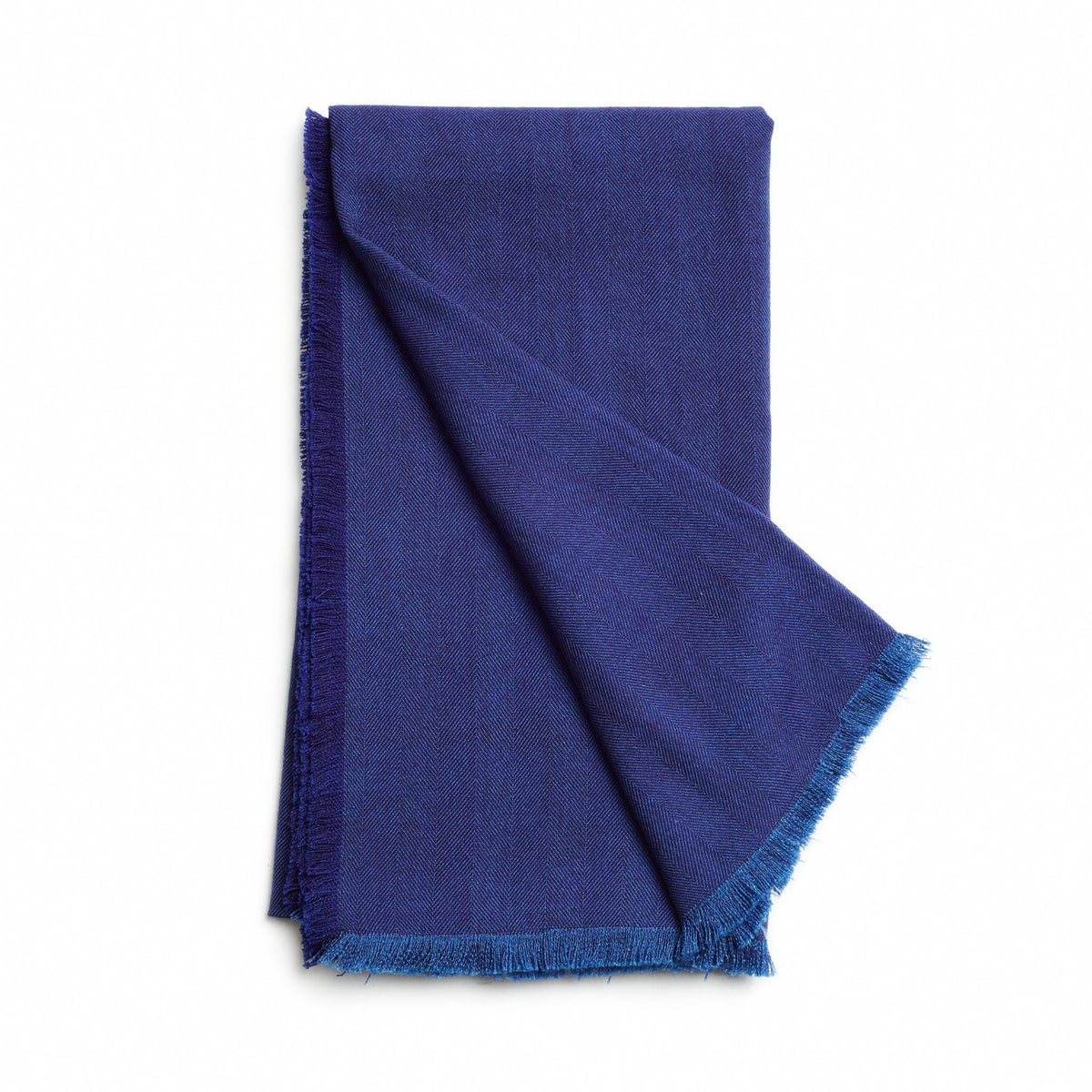 Folded deep blue color variation of the Variously merino throw with a contrasting blue fringed edge