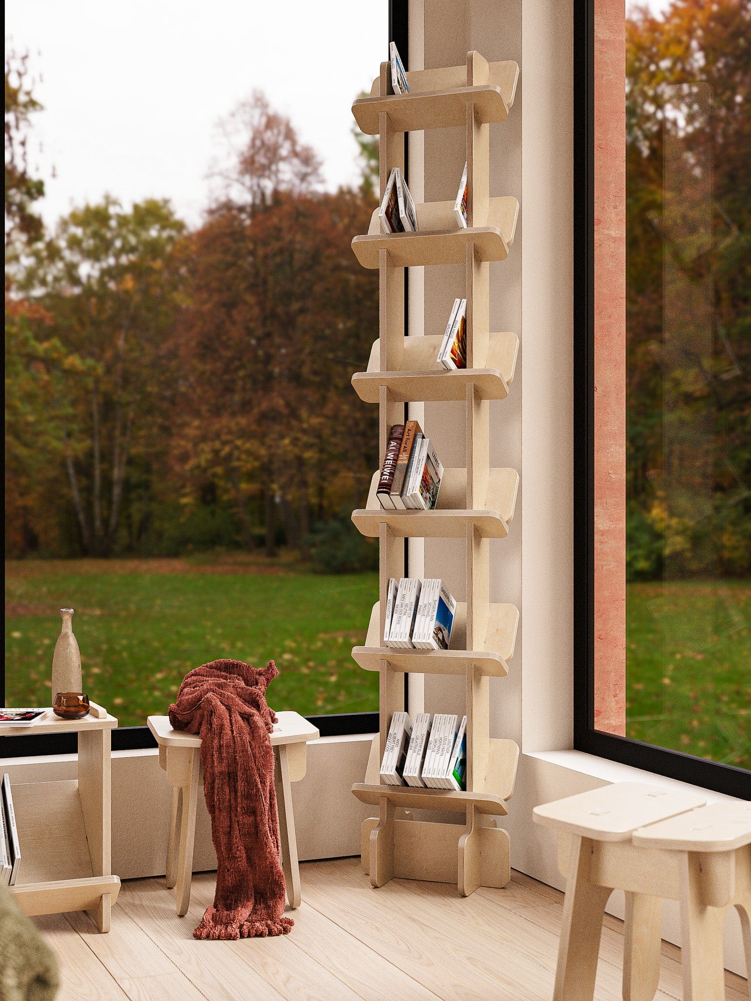 Yankel bookcase filled with books beside a large window overlooking autumn trees, with a rust-colored throw and stool nearby