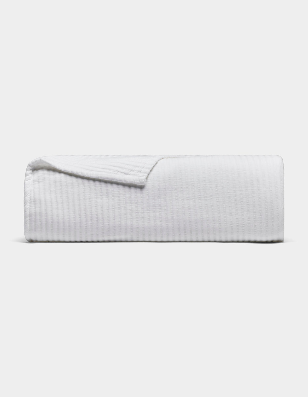 White Bamboo Coverlet folded on a pale background, with one corner turned back to reveal its fine ribbed texture and stitched edge.