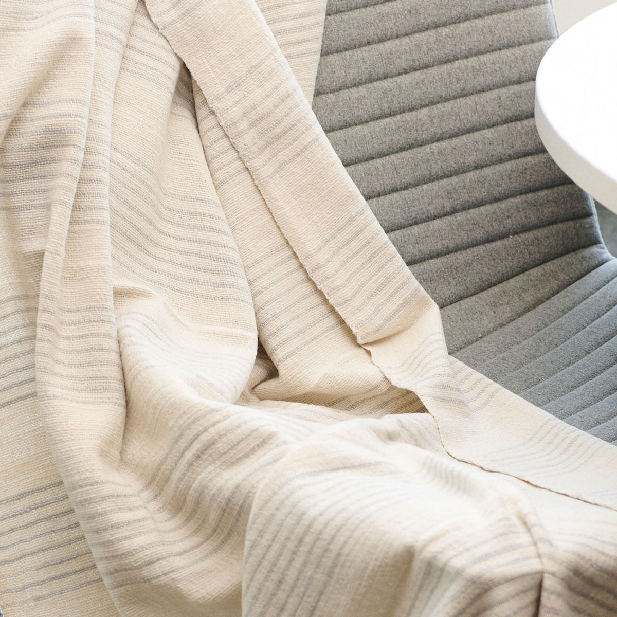 Silica Chalk off-white and gray striped throw gathered across a gray chair, highlighting its lightweight, fluid drape