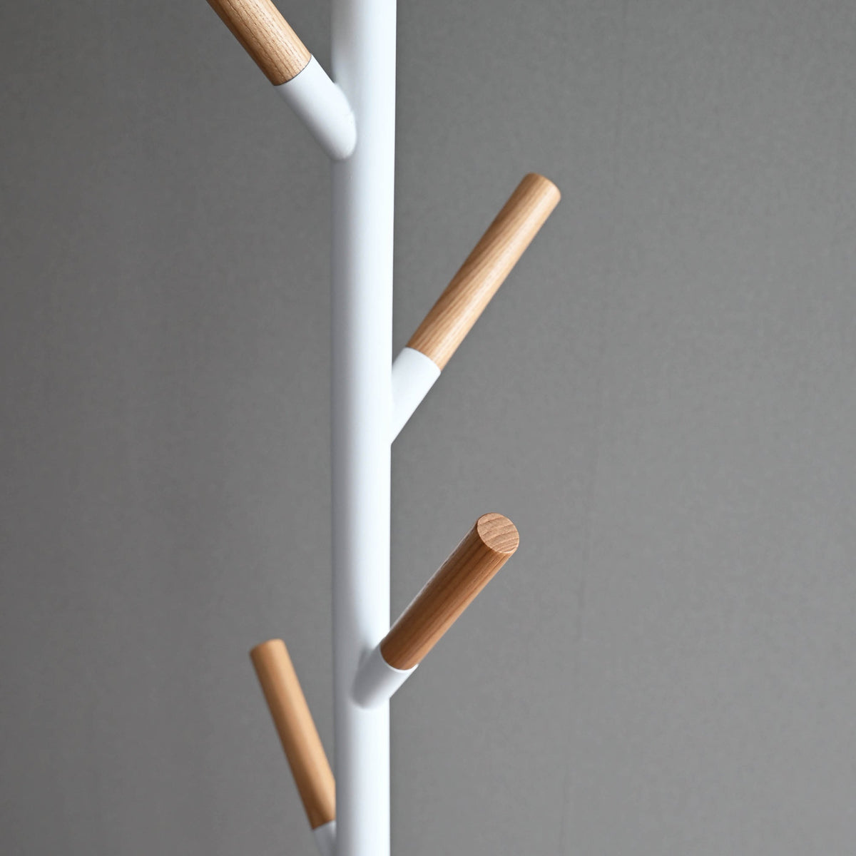 Detail of the white Yamazaki Home Coat Rack (70" H) - Steel, showing branches angled upward in different directions with smooth cylindrical light wood tips.