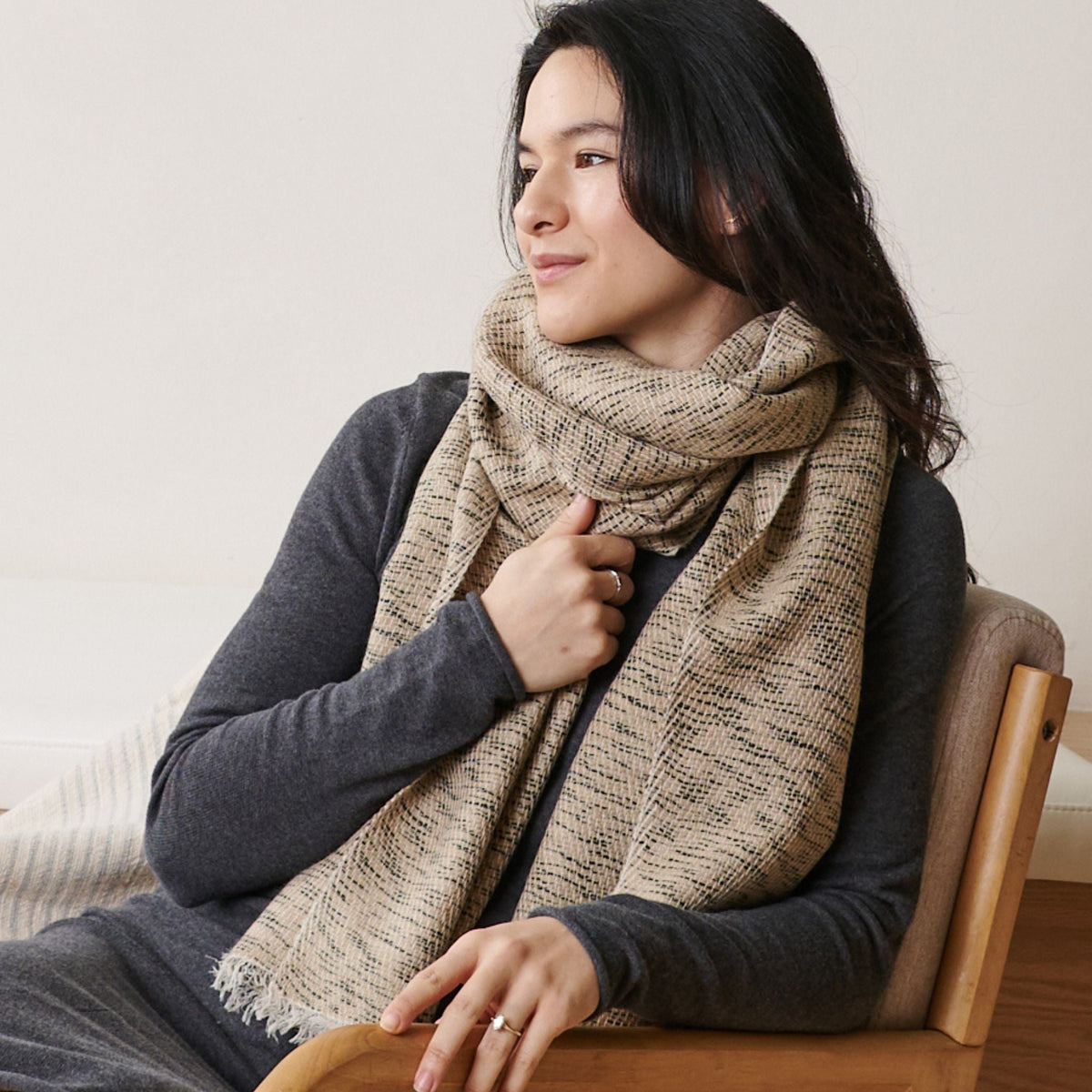 Close view of a seated woman wearing the thick beige scarf over a charcoal-gray top.