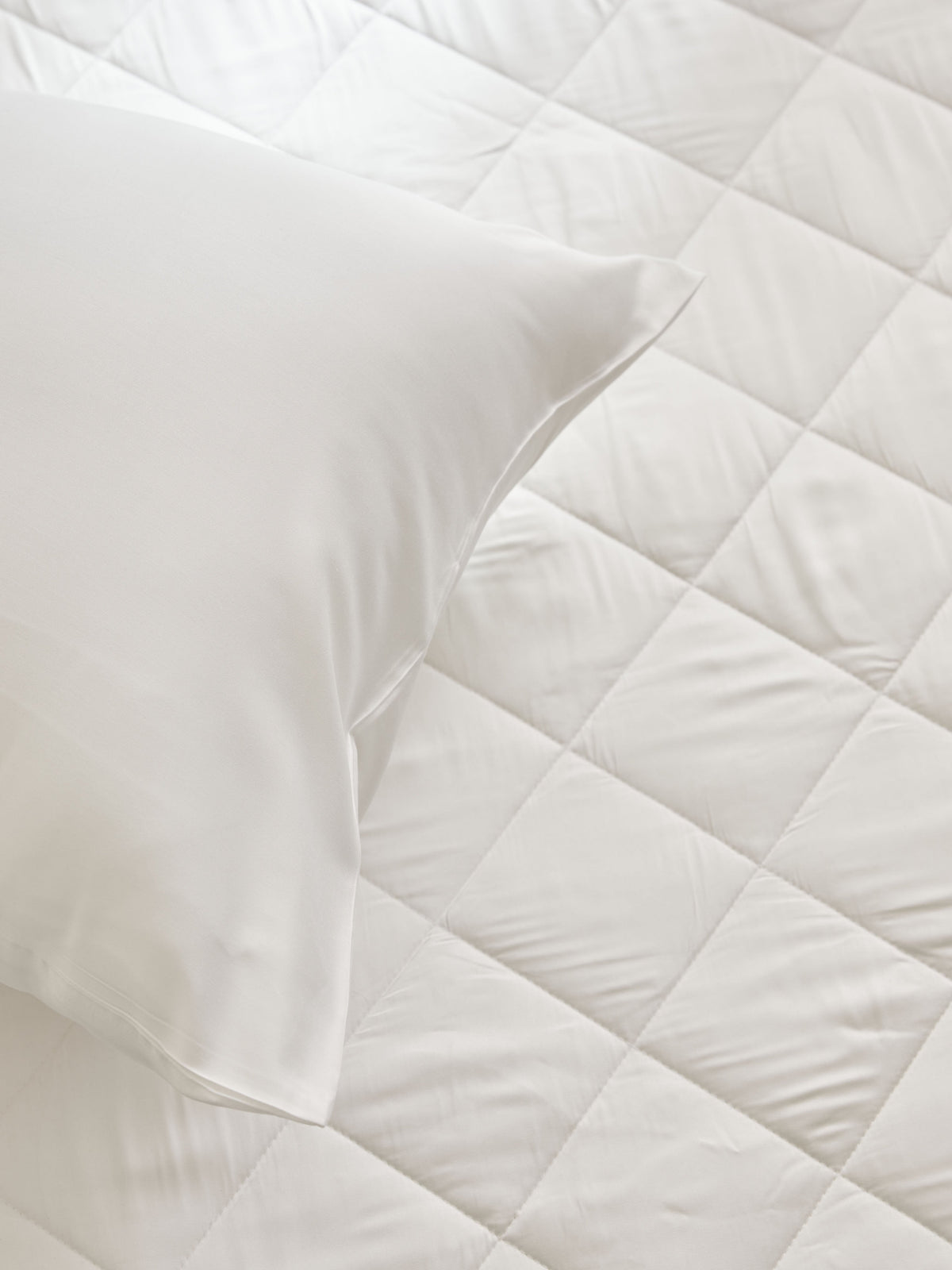 Overhead close-up of a white pillow resting on the mattress pad, showing its diamond-pattern stitching and gently cushioned surface.