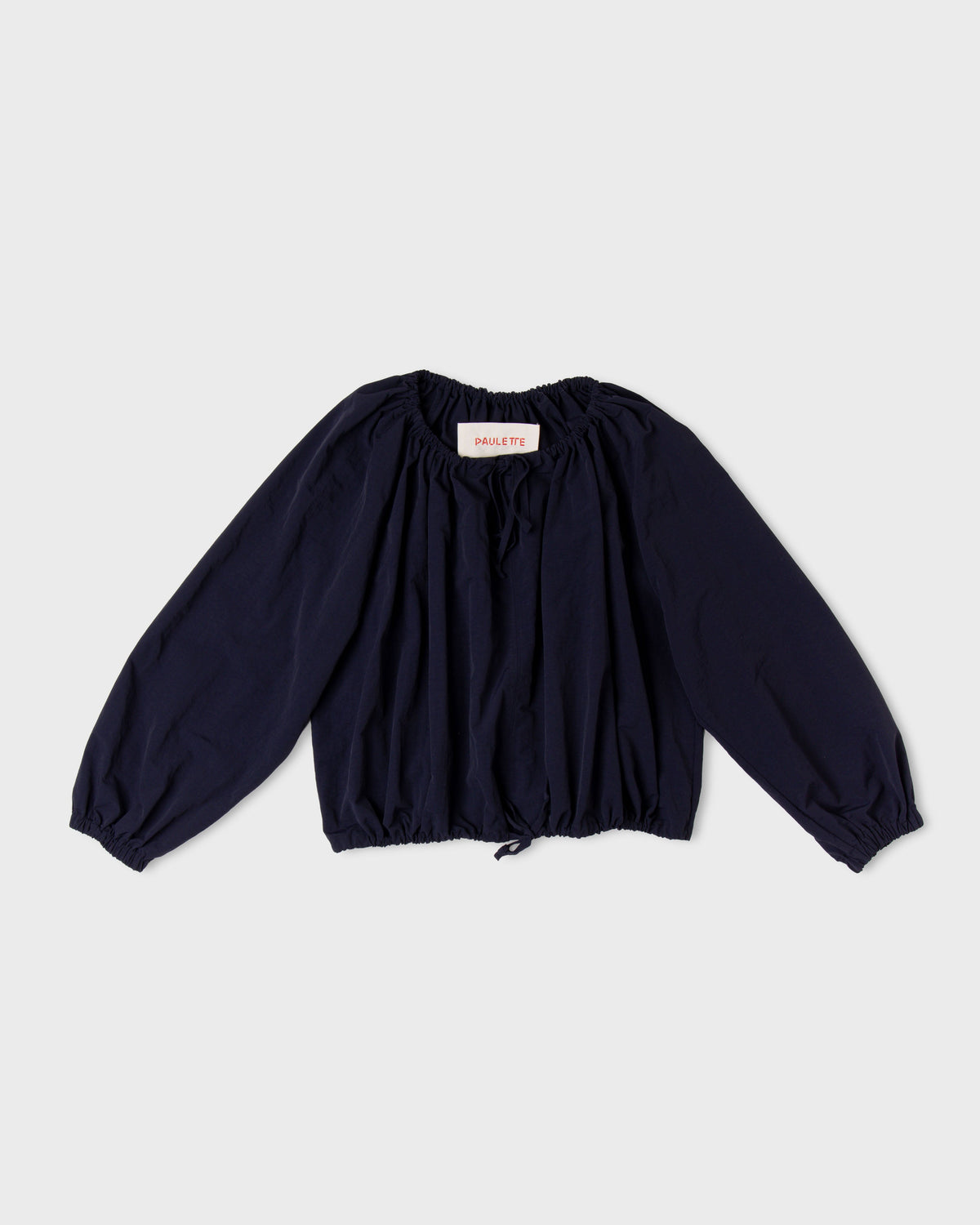 Dark navy Paulette Georgia Top displayed against a light background, showing a gathered neckline with front ties, voluminous long sleeves with gathered cuffs, and a cropped gathered hem with a center drawstring.