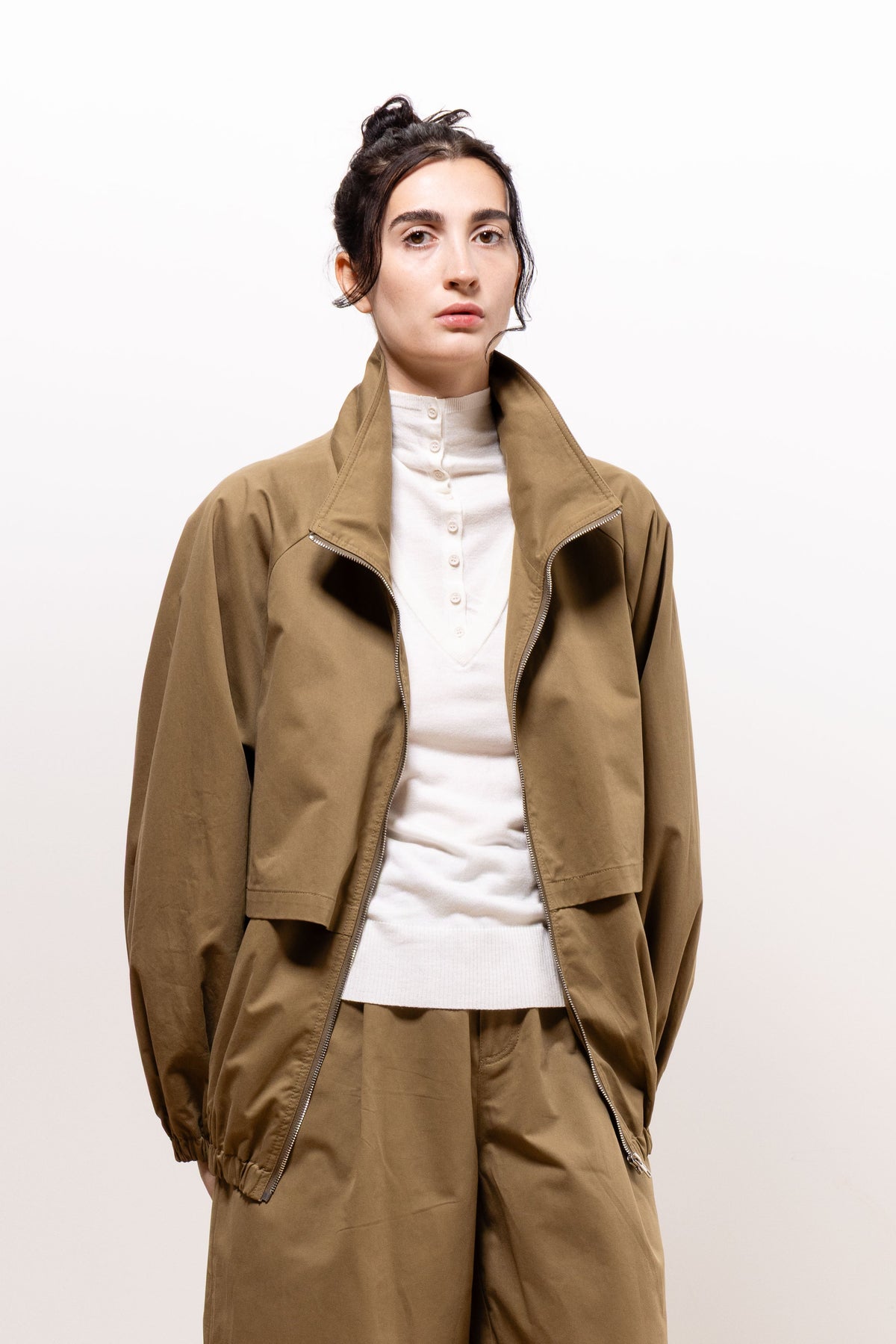 Model wearing the khaki-brown Paulette Lee Bomber Jacket open over a white high-neck top and matching trousers, showing its broad collar, loose fit, and gathered sleeve cuffs.