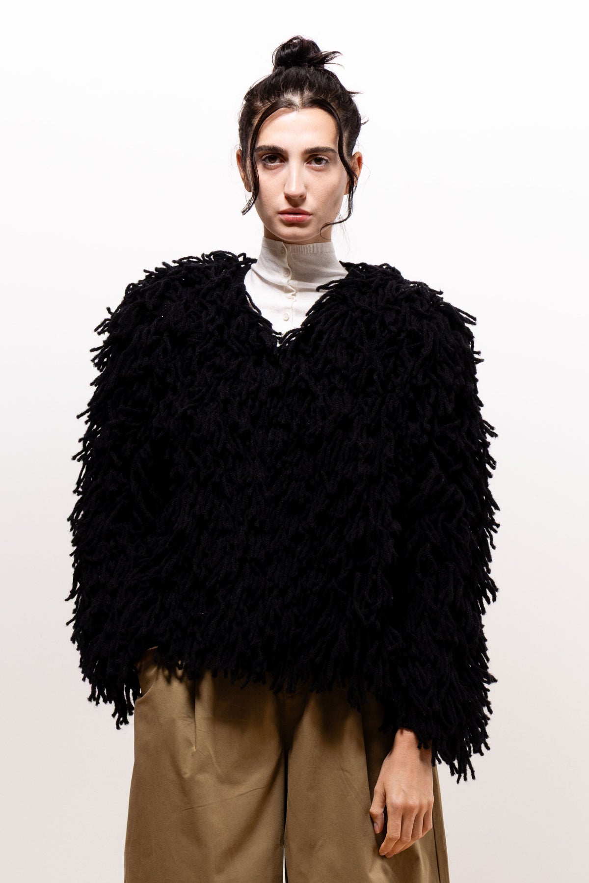 Front view of a model wearing the black Paulette Saint-Jean-de-Luz Cardigan over an ivory high-neck top and khaki-brown trousers, showing its voluminous texture and waist-length hem.
