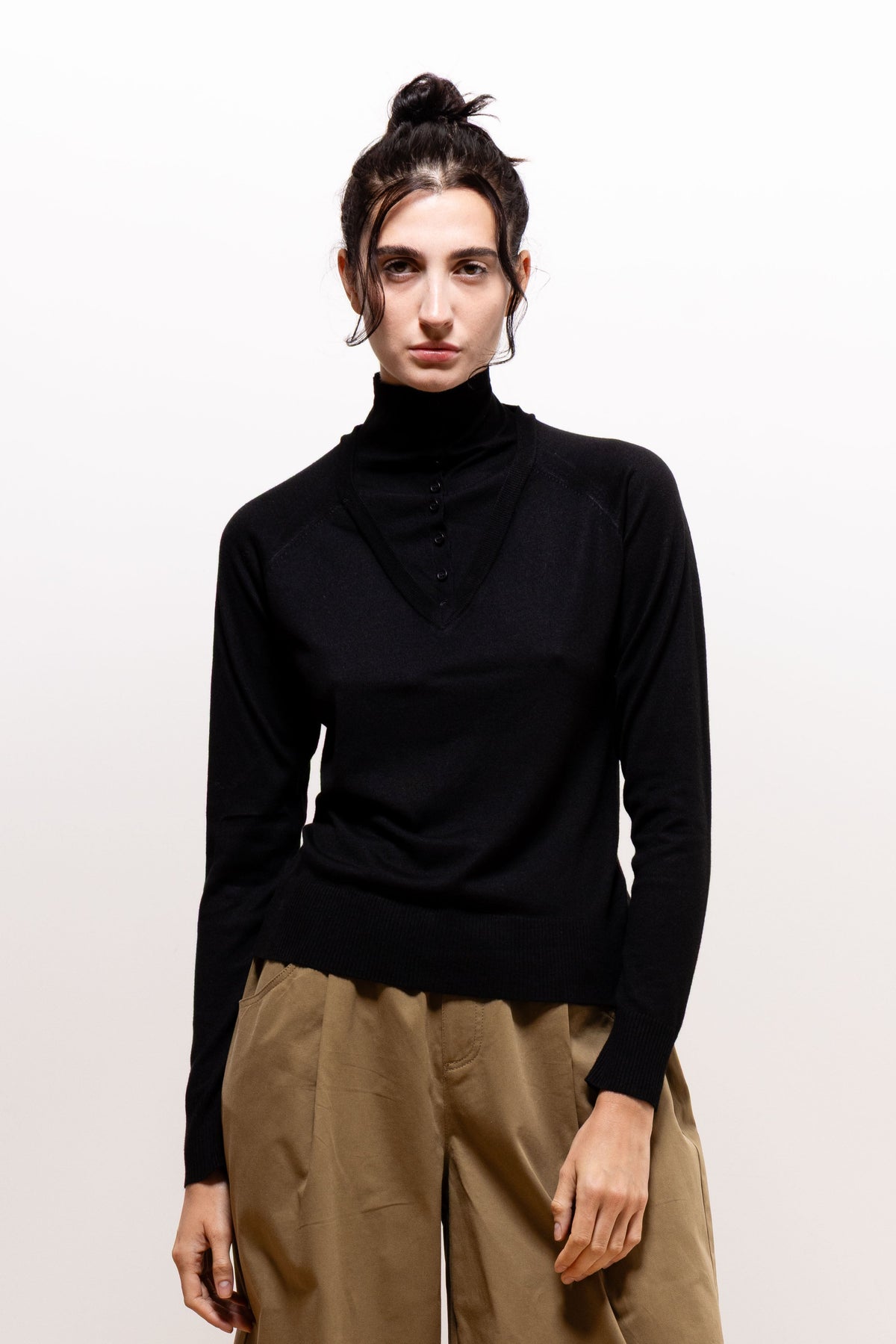 Front view of a model wearing the black Paulette Montagne Top with khaki-brown trousers, showing its long sleeves, fitted cuffs, and hem resting at the hips.