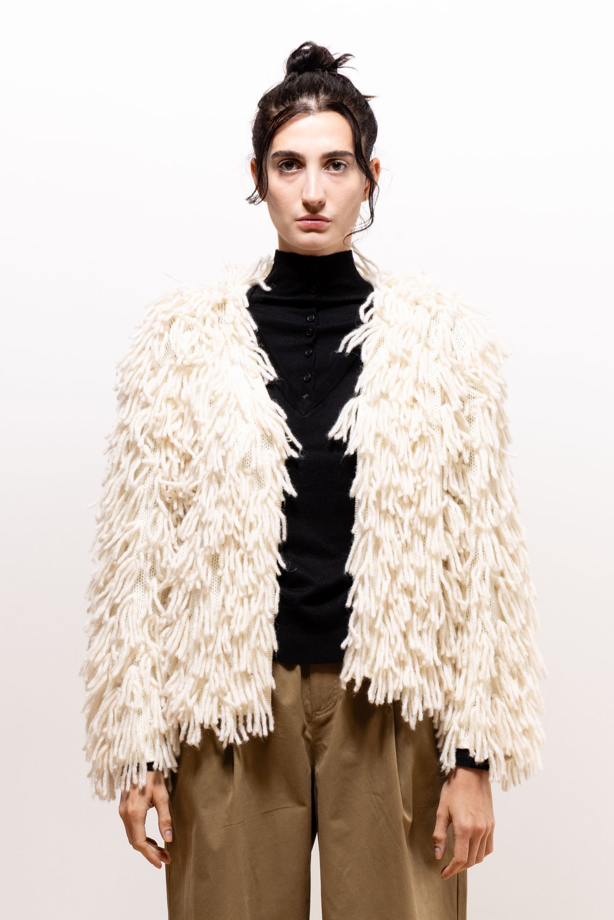 Front view of a model wearing the ivory Paulette Saint-Jean-de-Luz Cardigan with arms relaxed at her sides, showing its open front, dense strand-covered surface, and short hem.