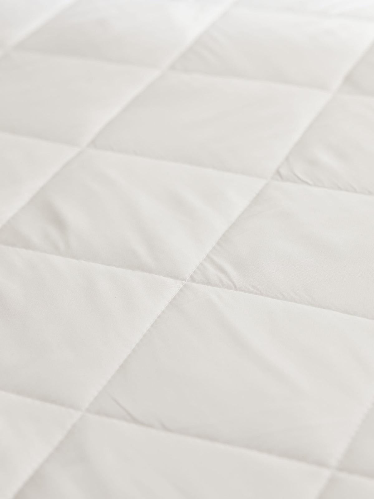 Close-up of the white mattress pad’s padded quilted sections, showing intersecting seams and subtle wrinkles in the fabric.