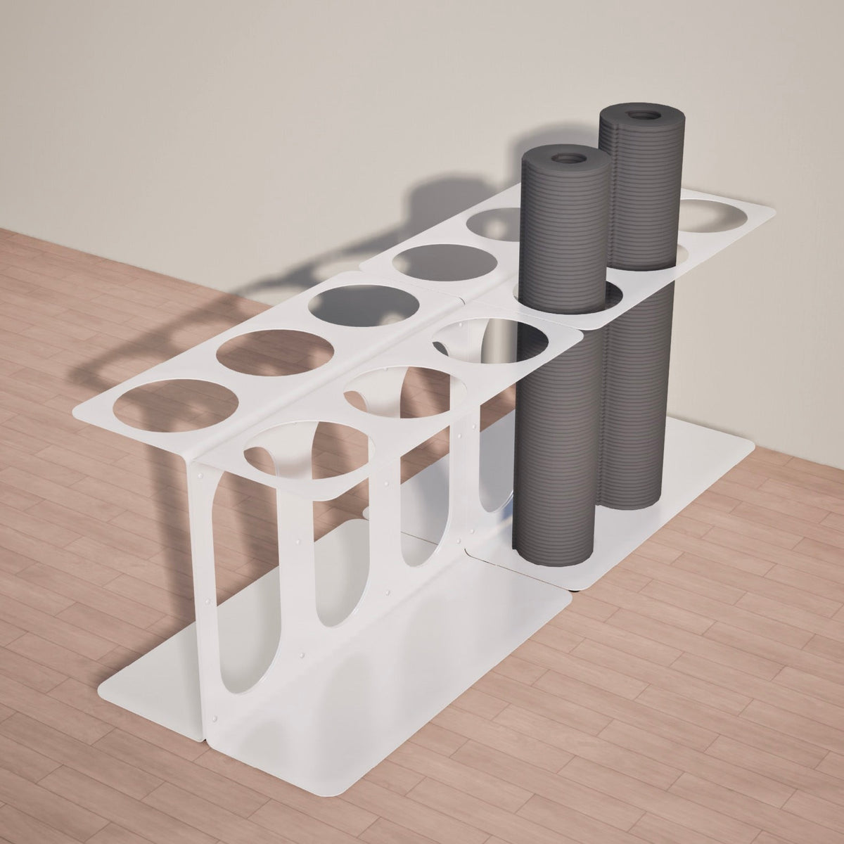 White metal floor stand holding three gray rolled mats or foam rollers, viewed diagonally from the front.