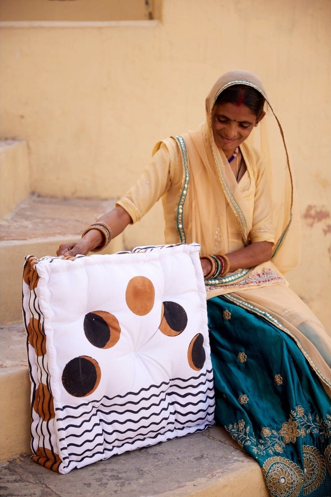 Woman holding a decorative pillow with a pattern of circles and wavy lines on a beige background.