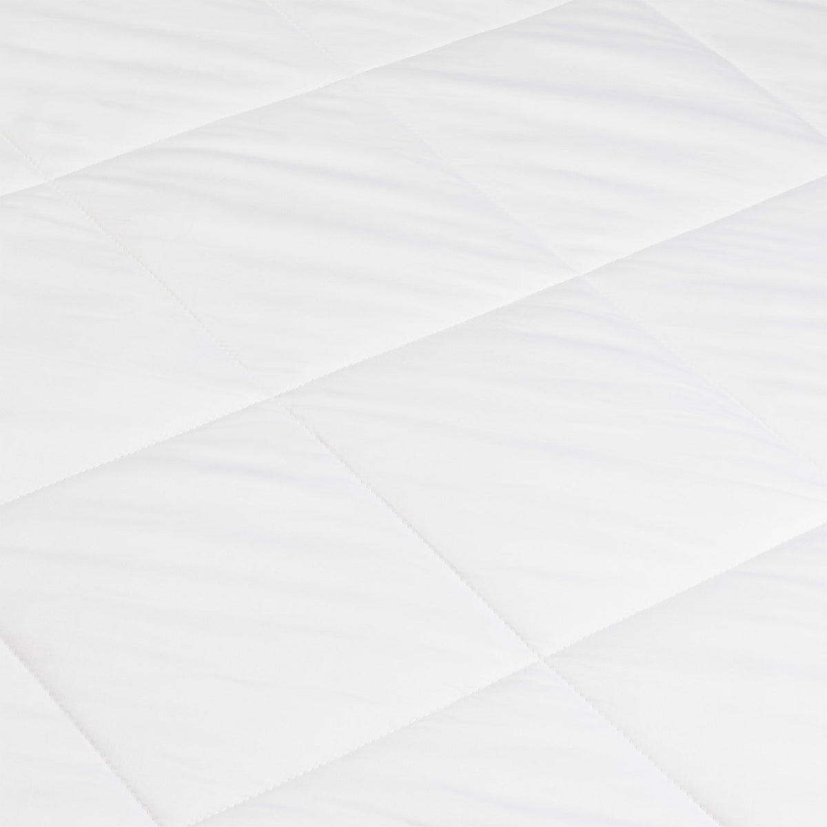 Close-up of the white comforter’s smooth fabric and intersecting diagonal stitching, forming large quilted sections.