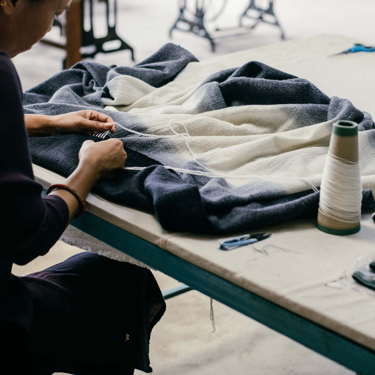 Artisans hand-finishing the Ink Black and White merino throw around a worktable with thread and sewing tools