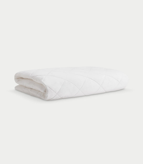 White Bamboo Mattress Pad folded on a pale background, showing its padded diamond quilting, rounded folds, and tucked fabric edges.