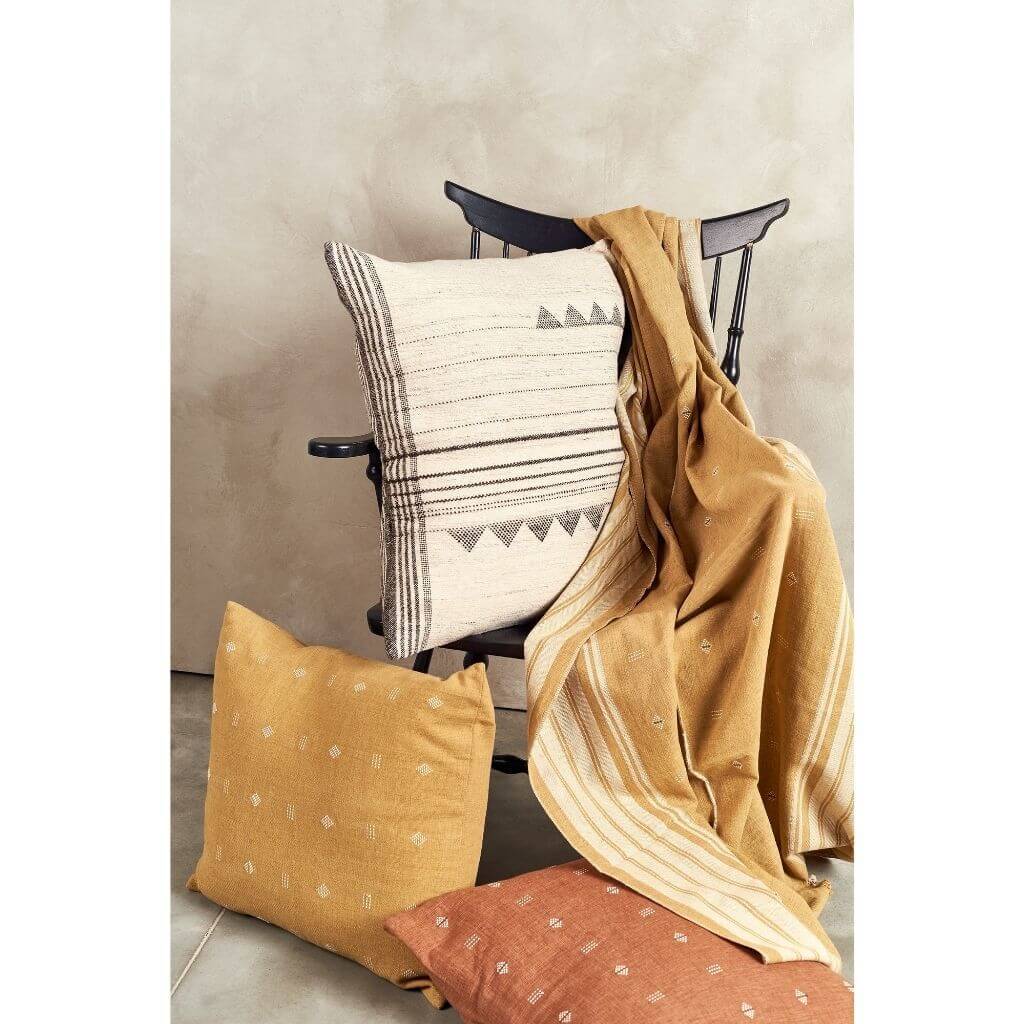 White and black pillow styled on a wooden chair with mustard textiles and coordinating cushions.