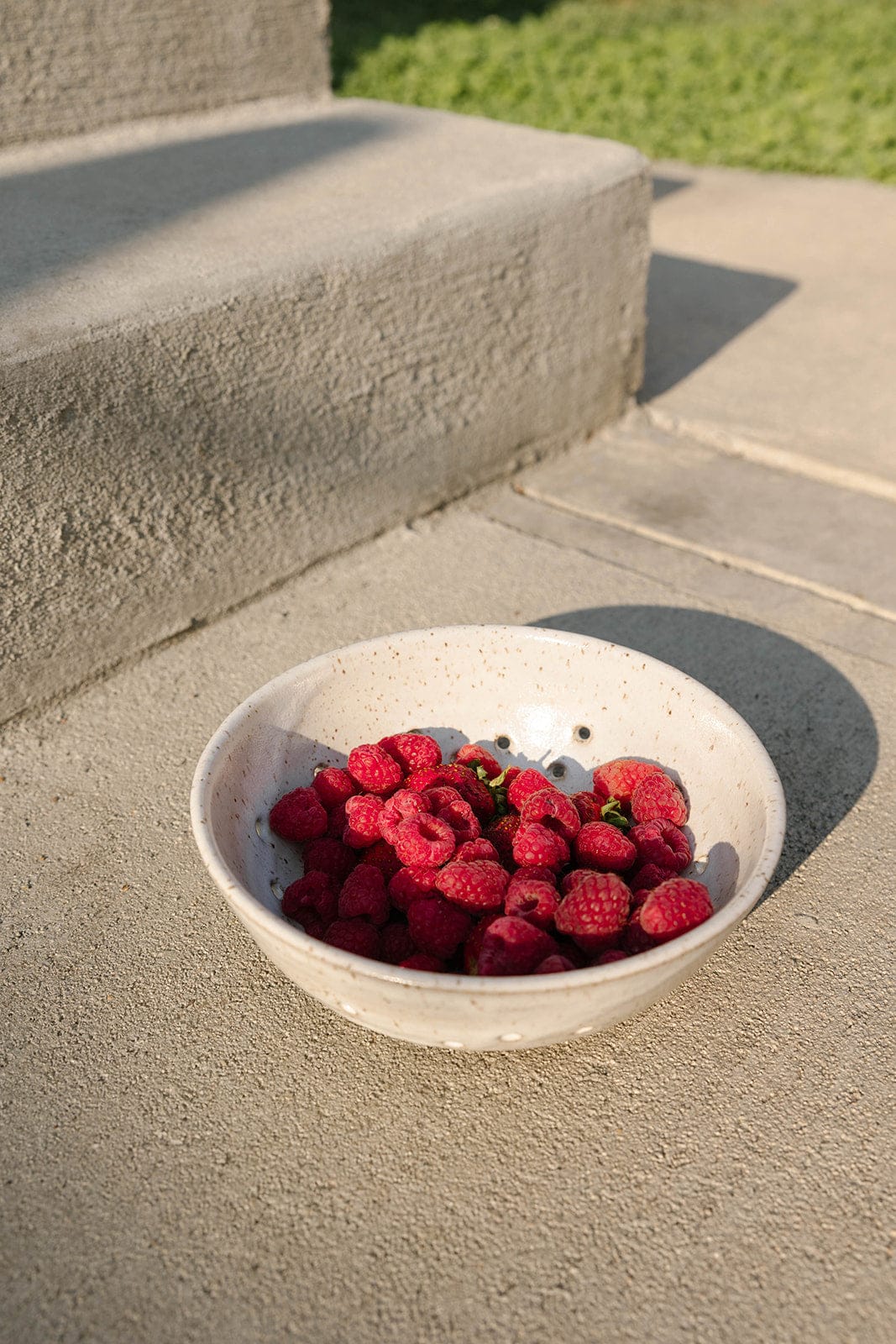 Bowl of raspberries on a concrete surface with grass in the background