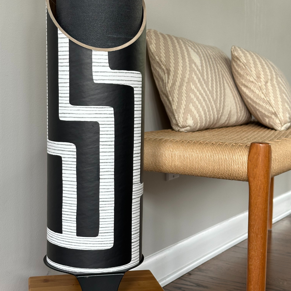 Close-up of the Colony tube beside a woven bench, highlighting its graphic white lines and finely textured black surface.