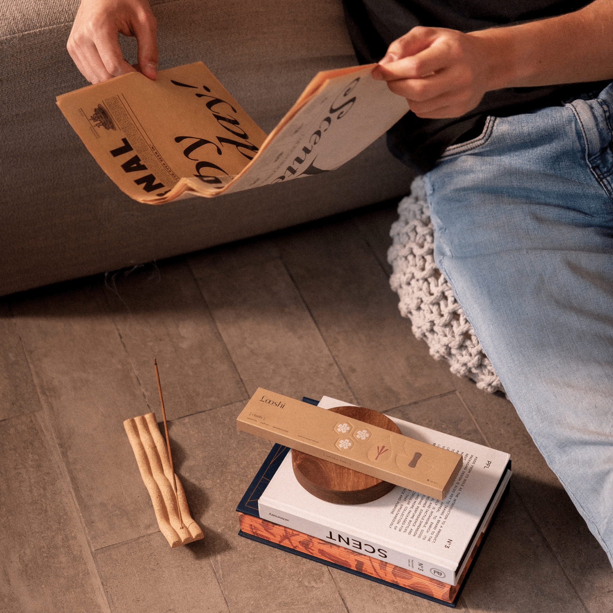 Person drawing on black paper beside a tan box of Looshi Clarify incense and several loose incense sticks