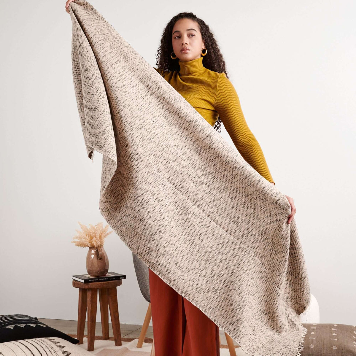 Woman holding the wide scarf open to display its generous size and textured neutral weave.