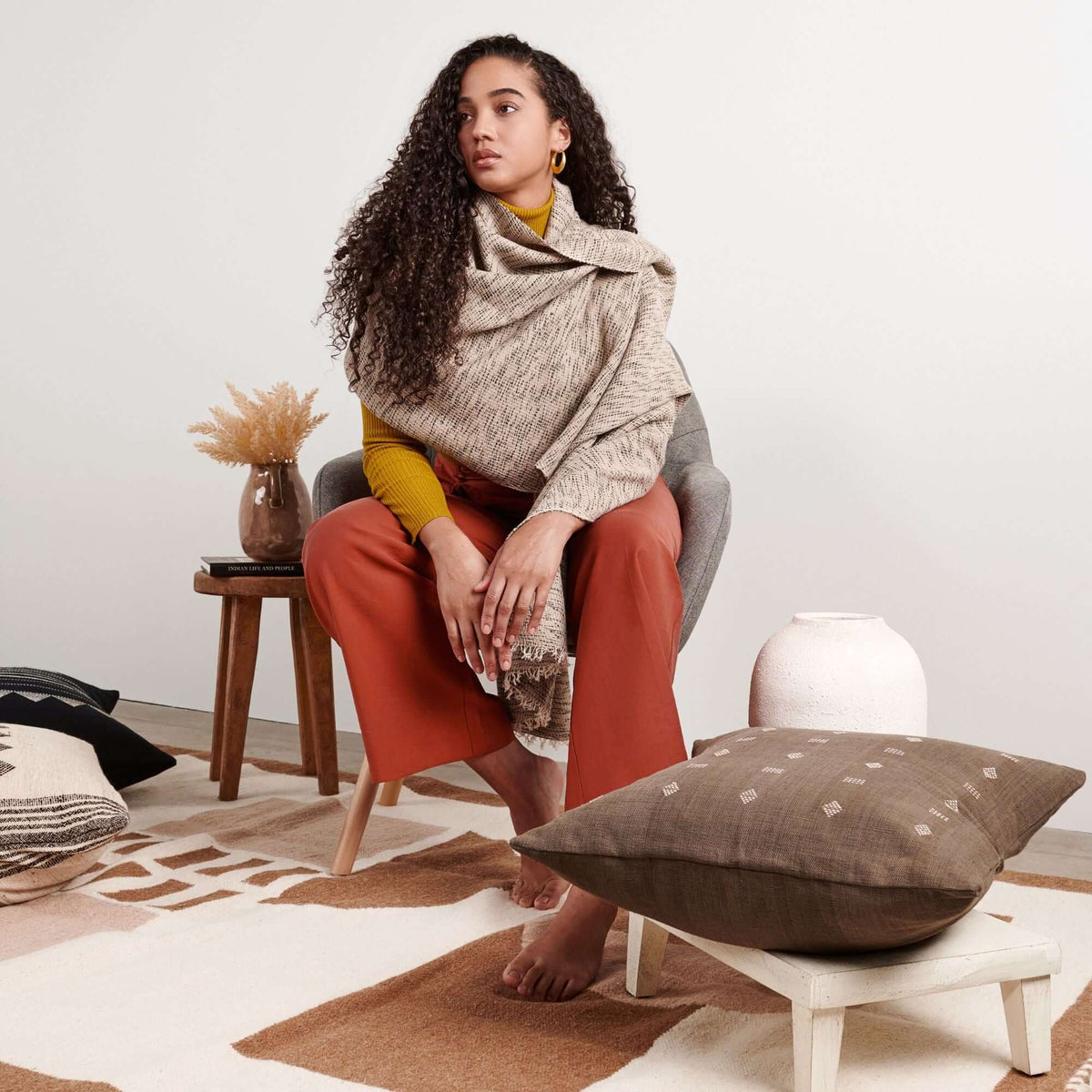 Woman seated in a styled studio interior with the scarf draped broadly around her shoulders.