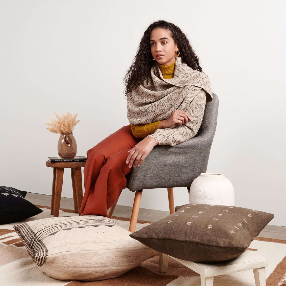 Seated woman wearing the scarf as a cozy wrap in a neutral studio setting.