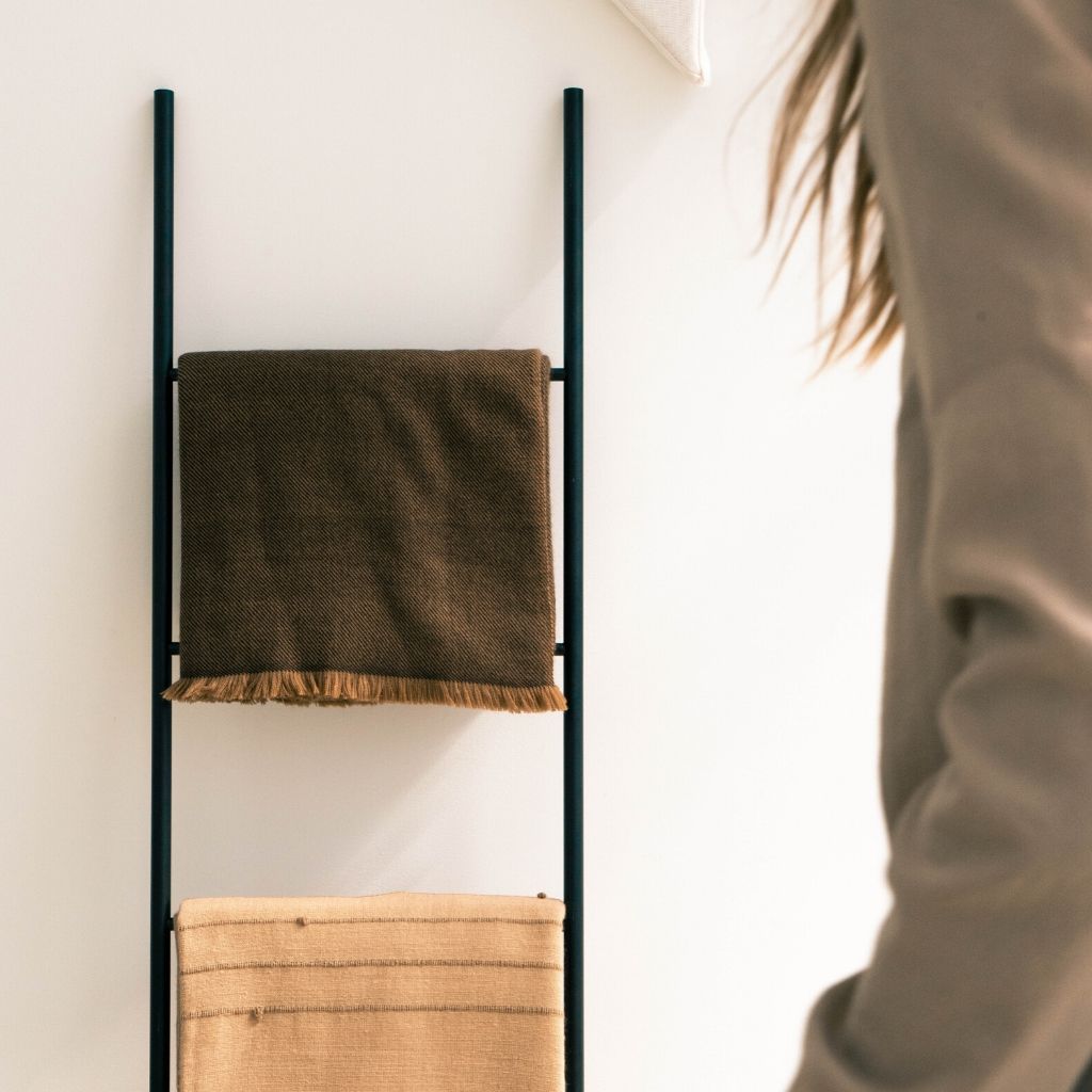 Folded Hay Brown merino throw displayed on a black blanket ladder above a woven storage basket