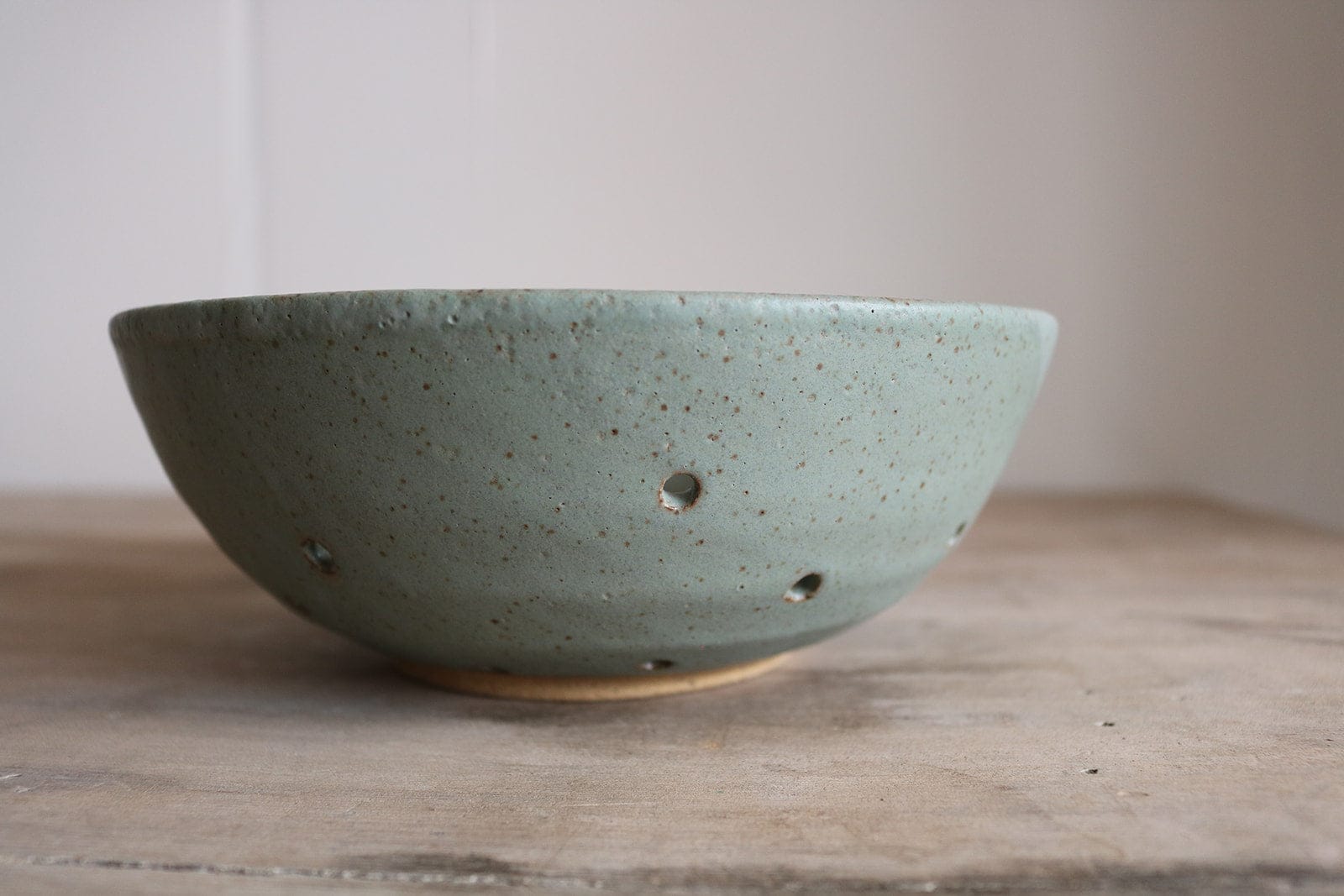 Green ceramic colander bowl on a wooden surface with a plain background