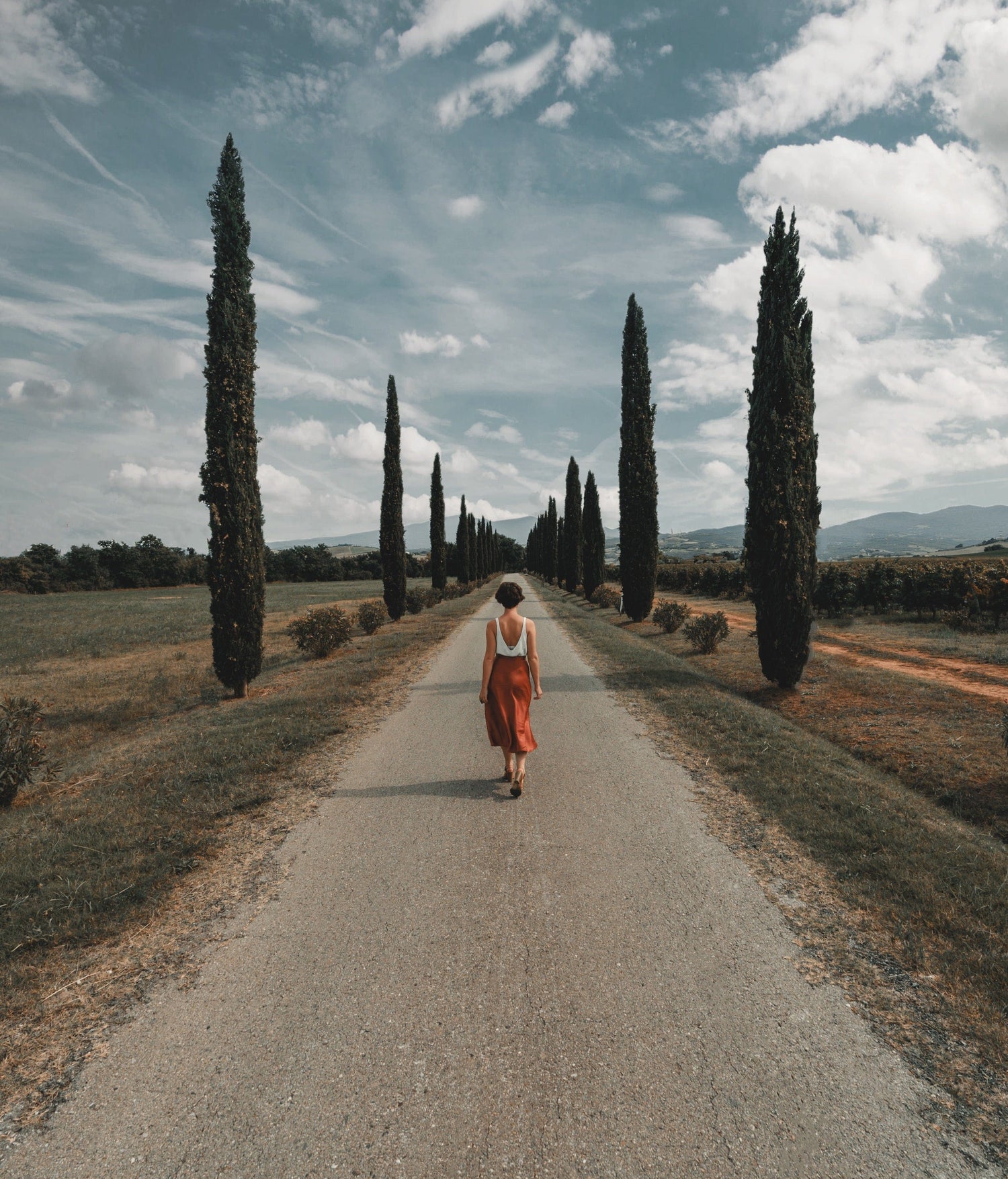 Woman walking down road with trees and sky