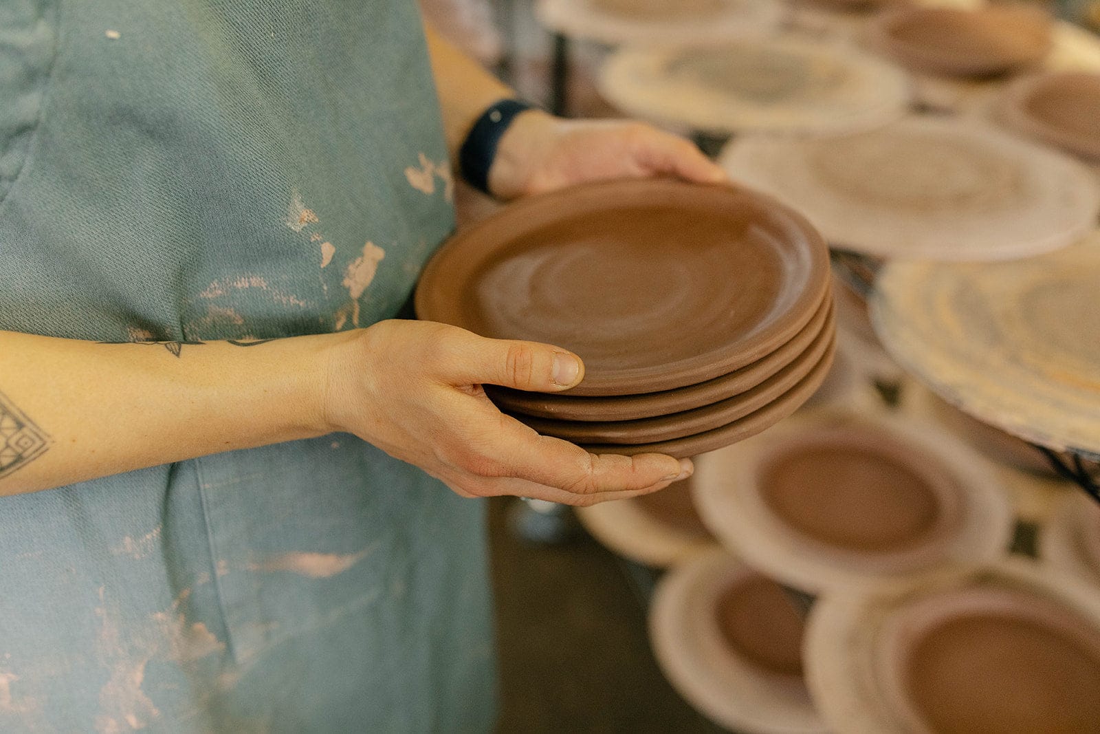Potter holding stacked handmade earthenware small plates in studio