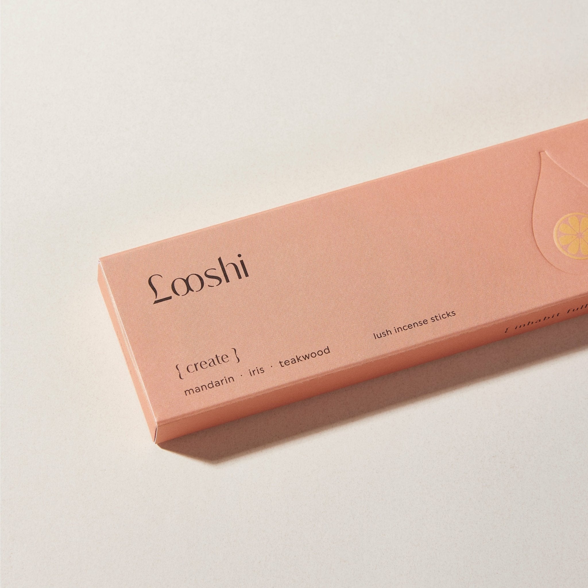 Peach-colored box of Looshi Create incense sticks on a cream surface, featuring mandarin, iris and teakwood fragrances