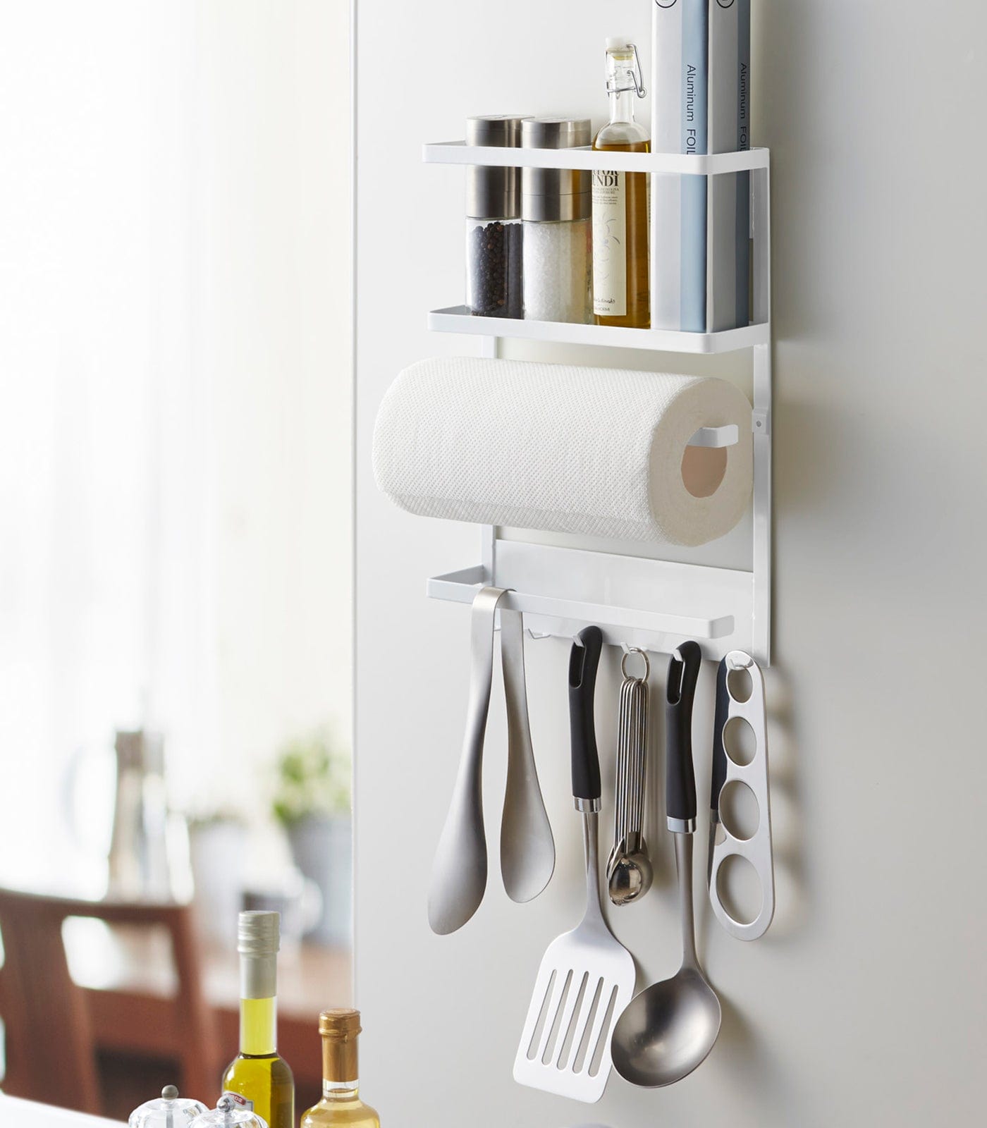 Wall-mounted kitchen organizer with utensils, paper towels, and bottles in a kitchen setting.
