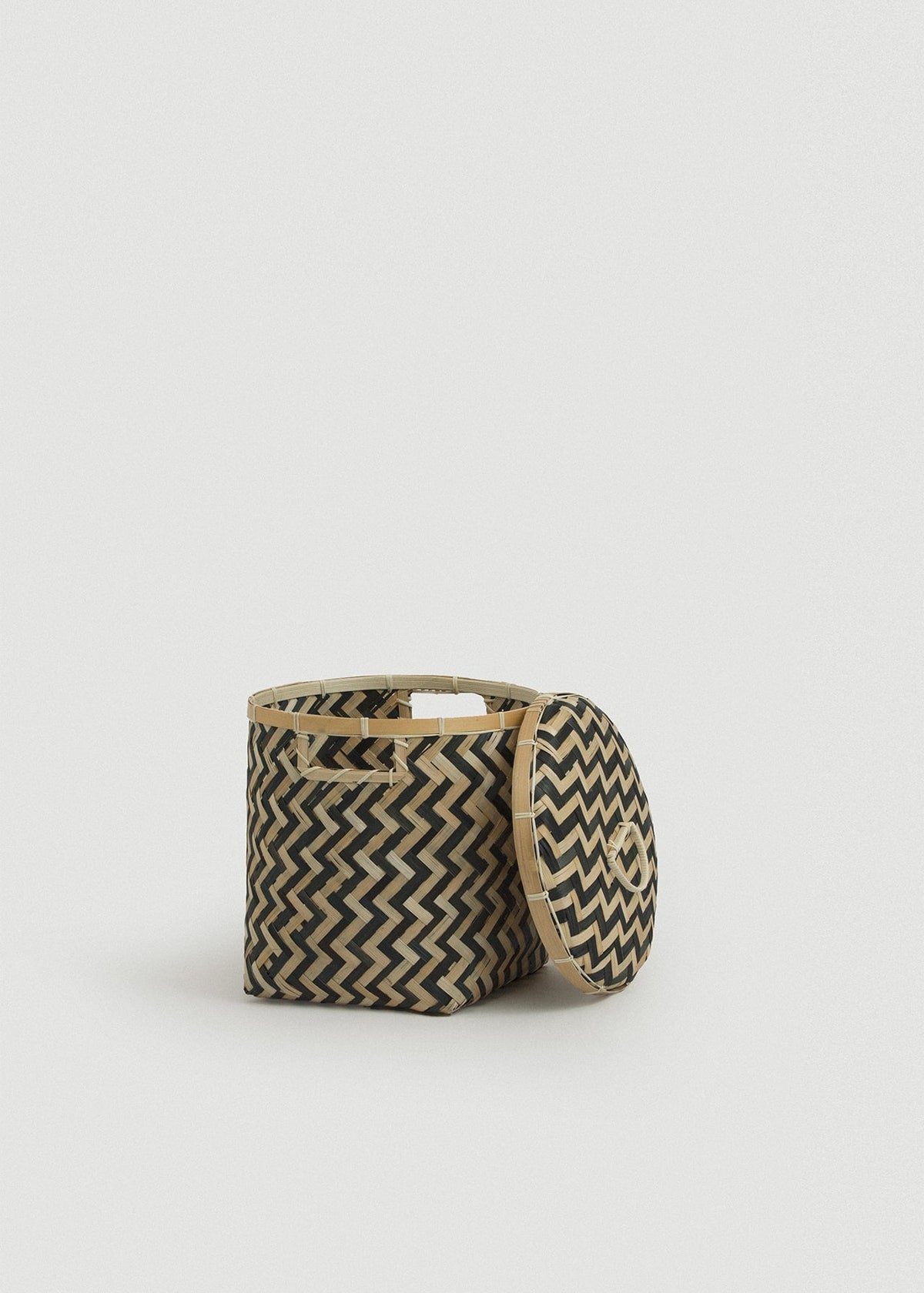Small open bamboo basket with its matching woven lid leaning against the side.