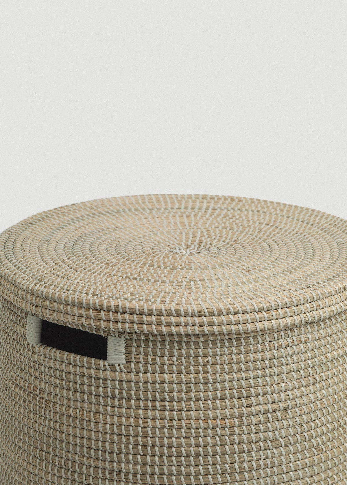 Close-up of the spiral-woven flat lid, basket rim, and black rectangular handle.
