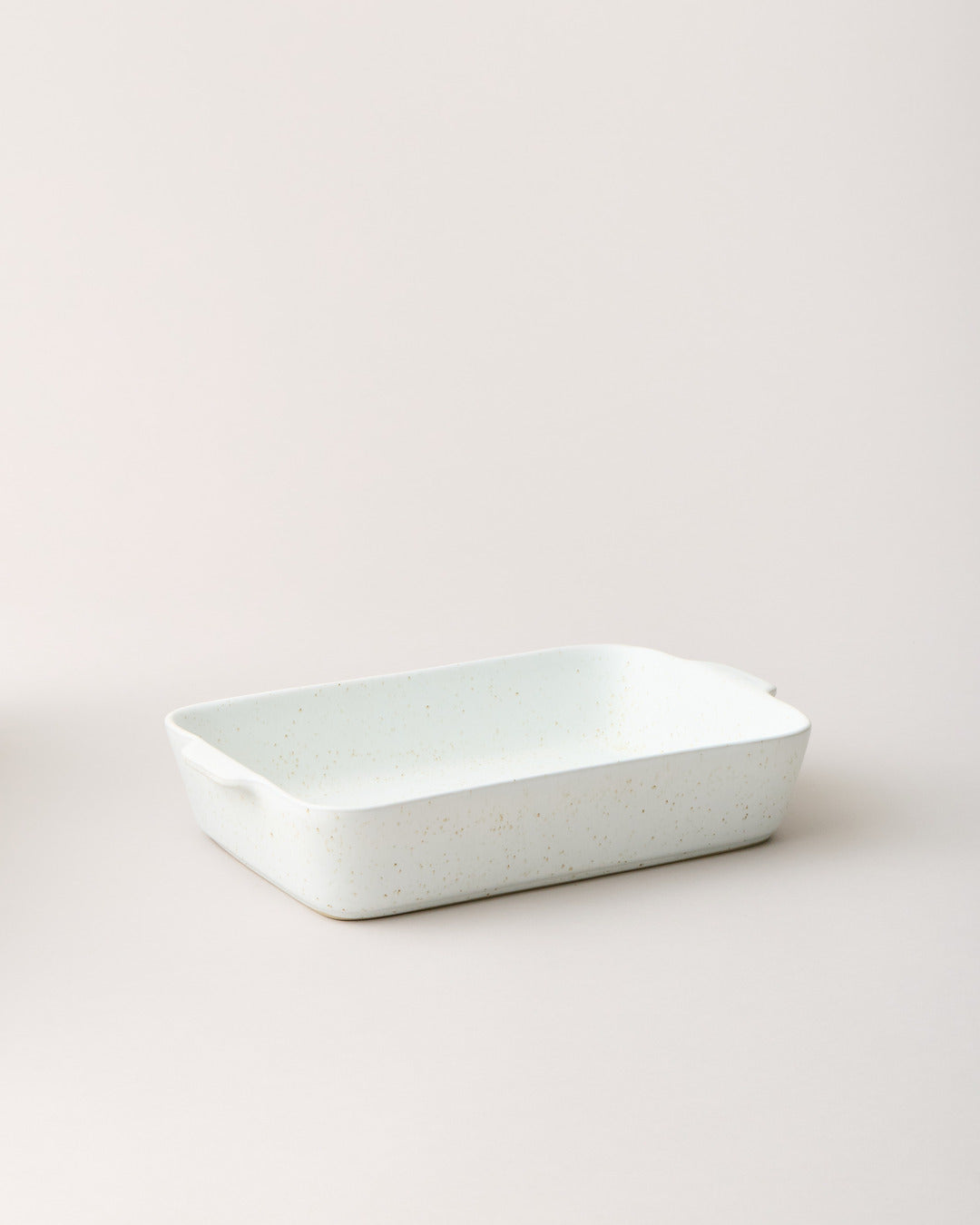 Empty speckled white Fieldstone Baker shown at a low angle, with a shallow rectangular basin, rounded corners, and small side handles.
