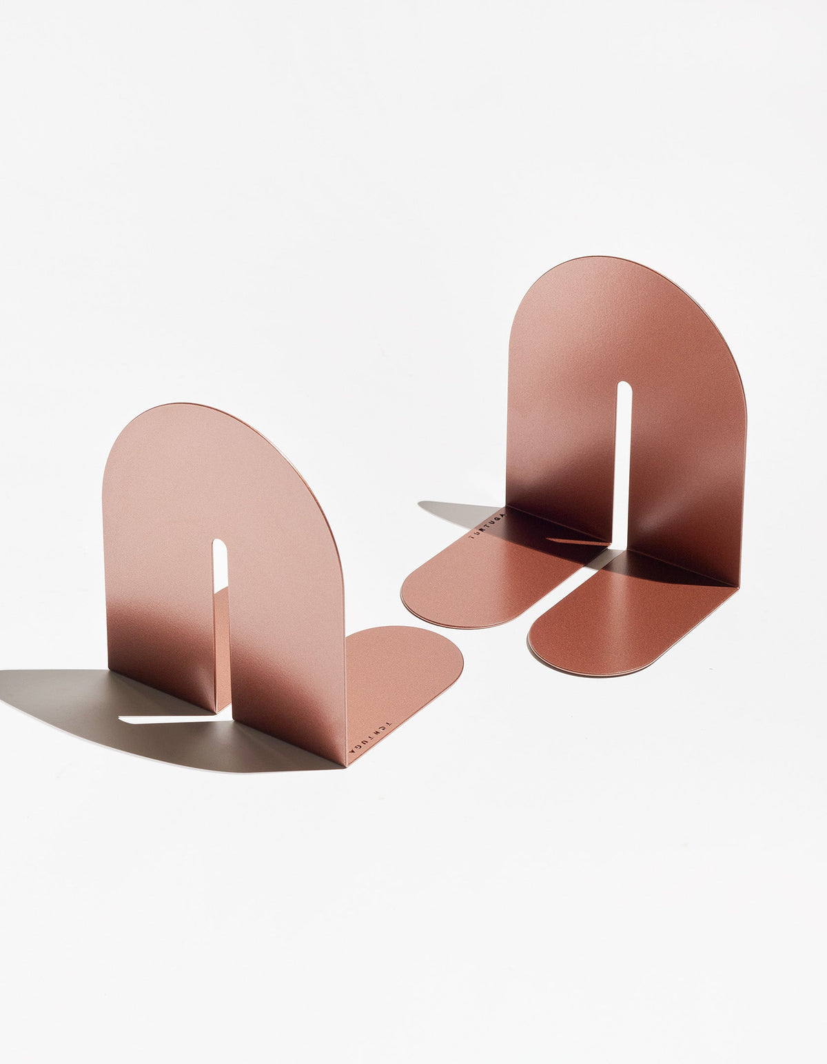 Copper-coloured Tortuga Forma Dumbo Bookend Pairs - The Architect Collection viewed at opposing angles on white, showing reflective curved panels, narrow slots and rounded bases.
