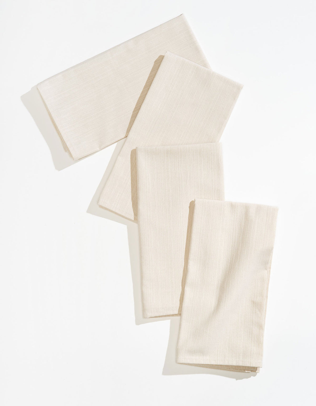 Four ivory Tortuga Forma Dinner Napkins Sabi folded into rectangles and loosely overlapped on white, showing softly creased fabric and narrow stitched hems.