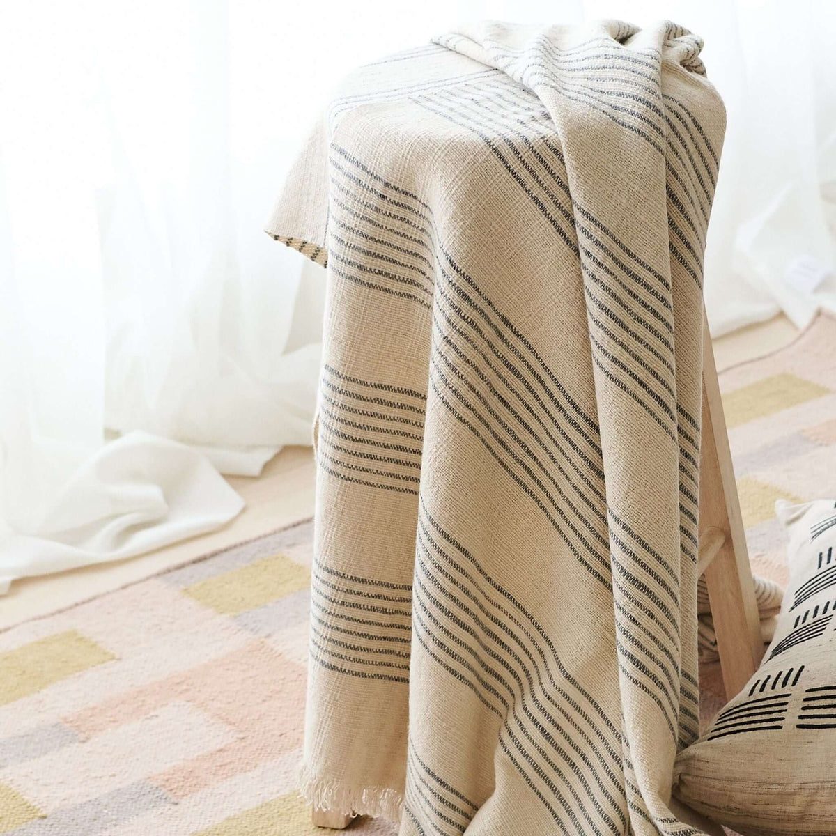 Silica Chalk off-white throw cascading over a chair, showing grouped vertical gray stripes and a softly fringed edge