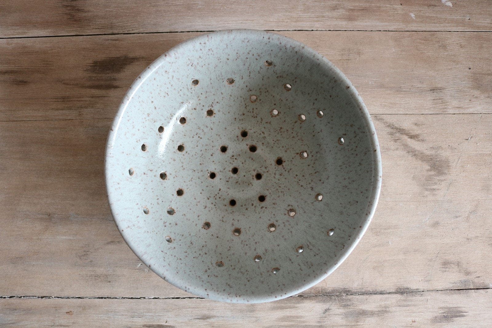 Speckled ceramic colander on a wooden surface