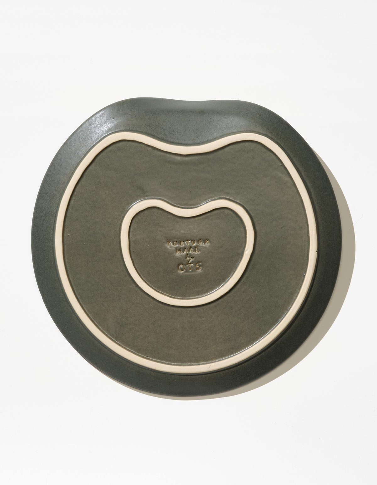 Underside of Tortuga Forma Dinner Plate Single in Liche, showing two cream-coloured raised outlines following its irregular shape and a central maker’s mark that is too small to read.