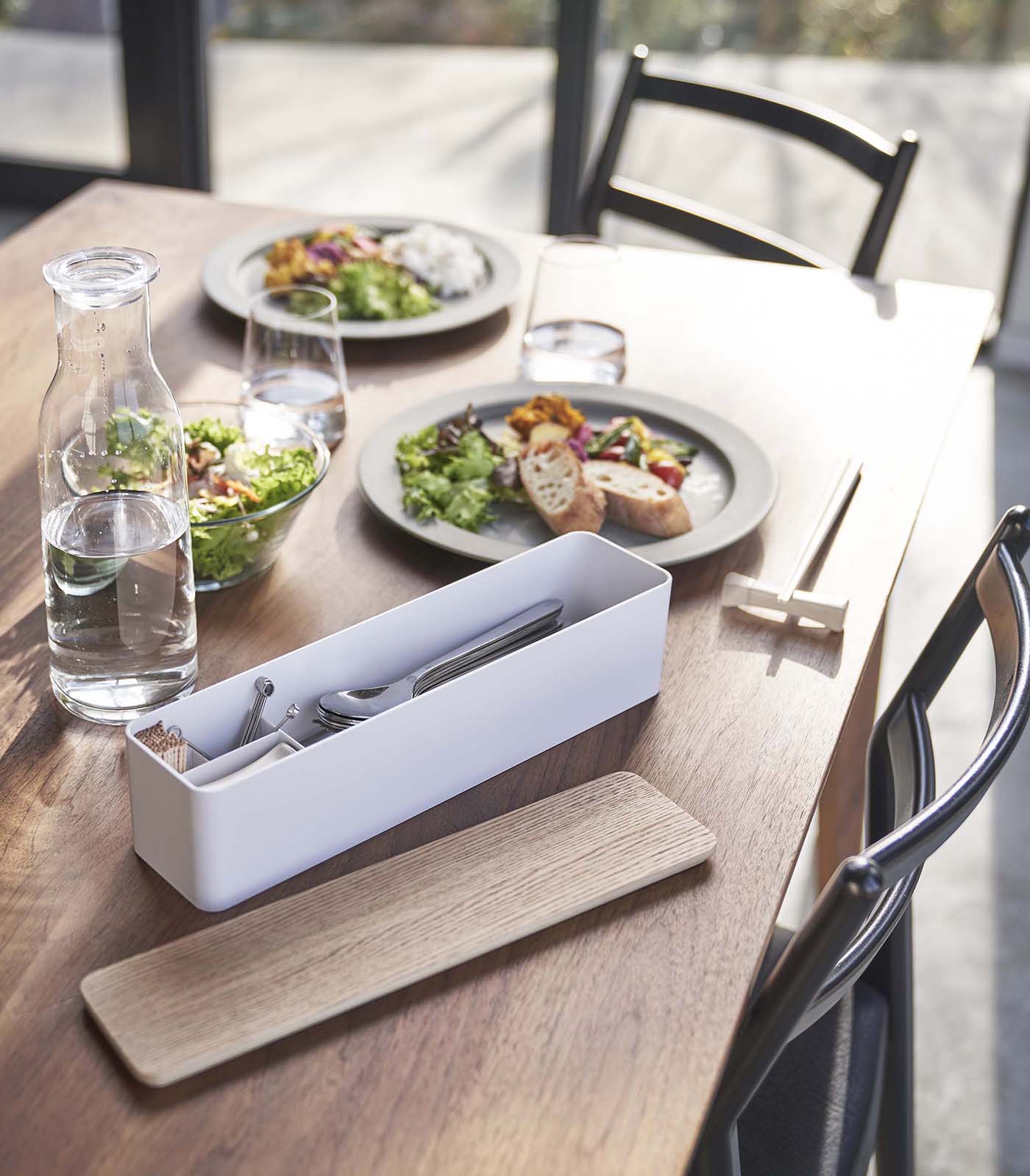 Table setting with plates of food, glasses, and a white utensil holder on a wooden table. and a Utensil Case.