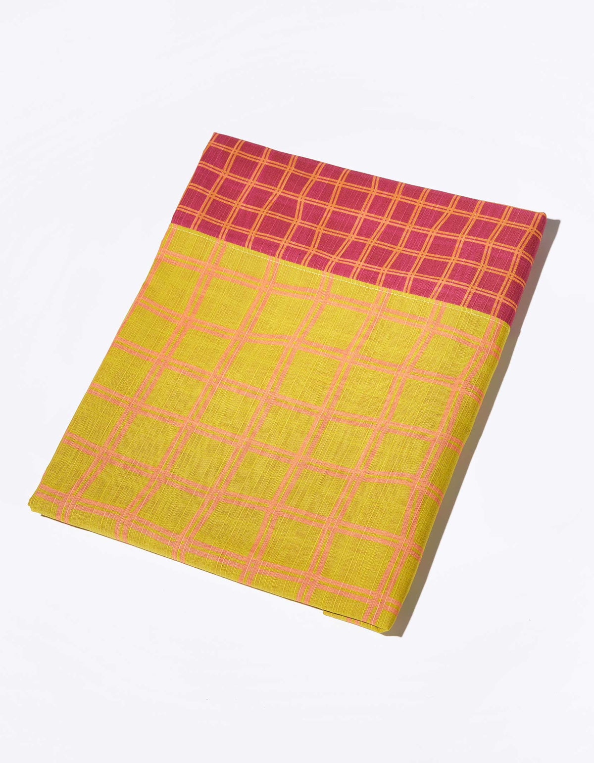 Folded Tortuga Forma Tablecloth Reversible Grid on white, showing mustard-yellow fabric crossed by pink lines, a contrasting burgundy grid border and neatly finished edges.