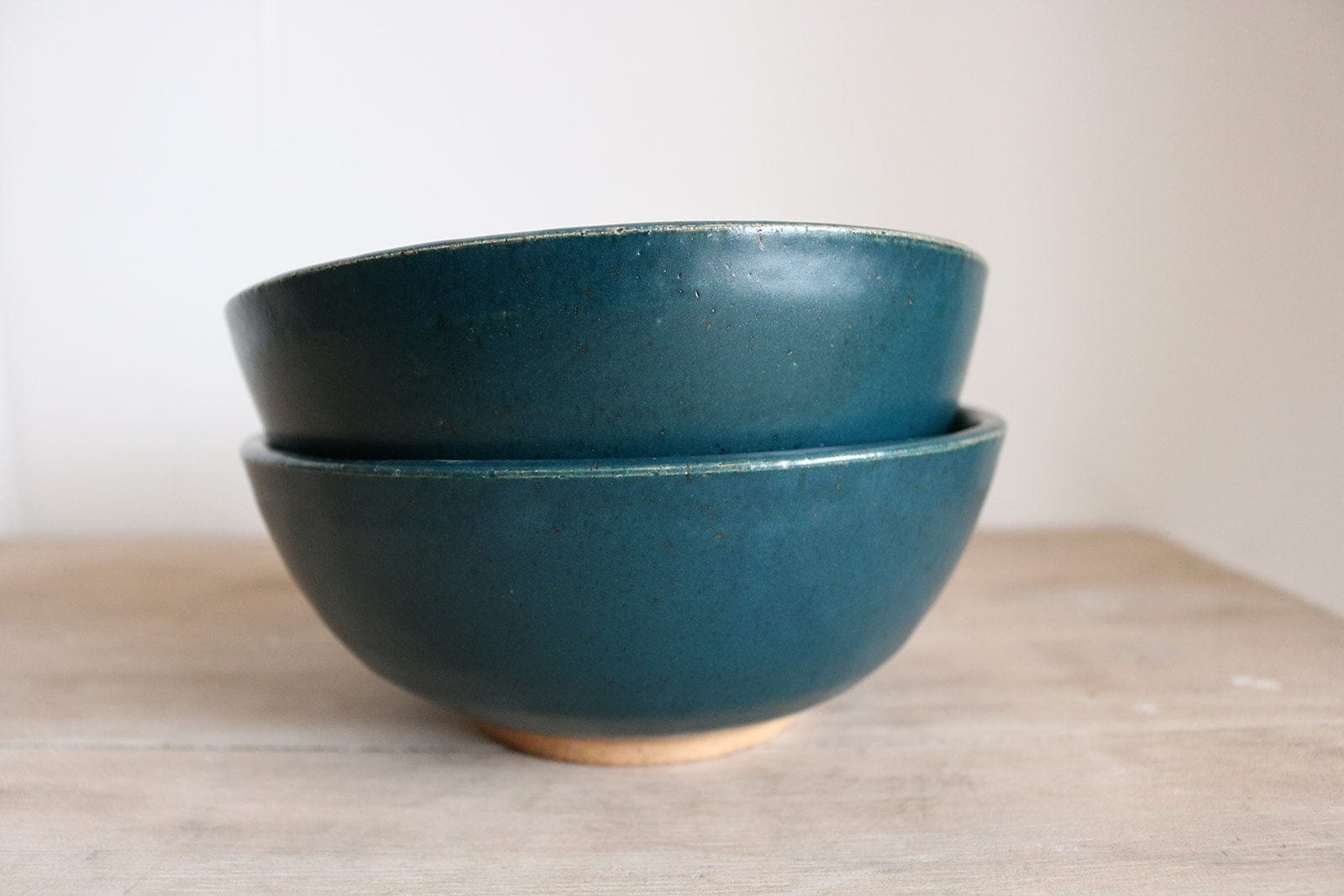 Two blue ceramic bowls stacked on a wooden surface with a white background