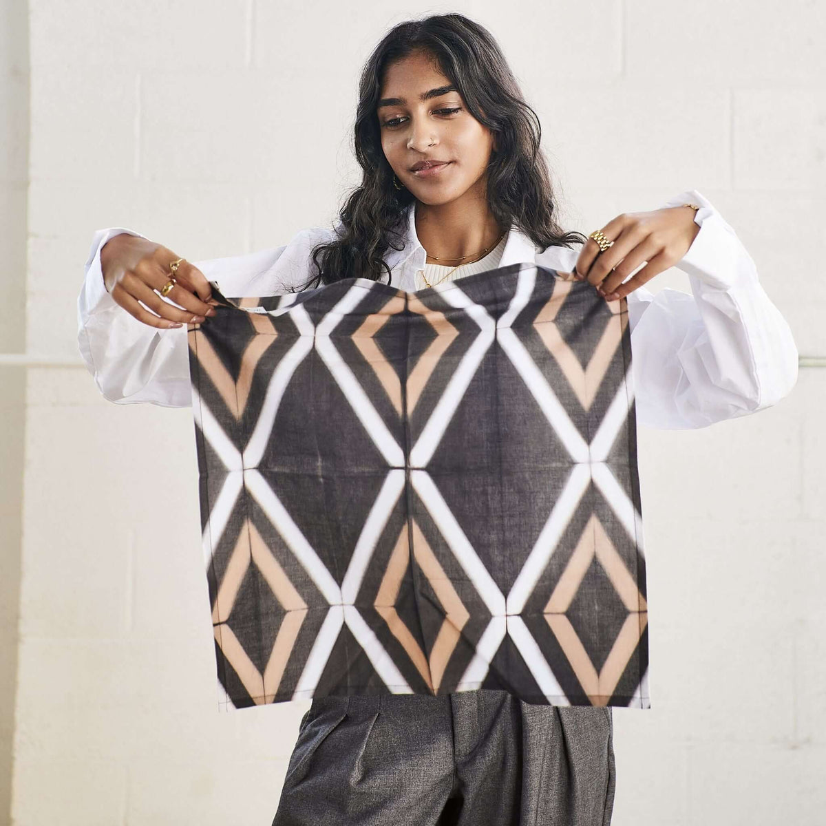 Woman displaying the full square napkin and its repeating geometric diamond design.