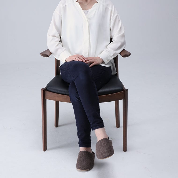 Person sitting on a chair wearing white shoes with a neutral background, As shown: Sakura wood, Medium Brown finish, Black leather. WING Side Chair by CondeHouse