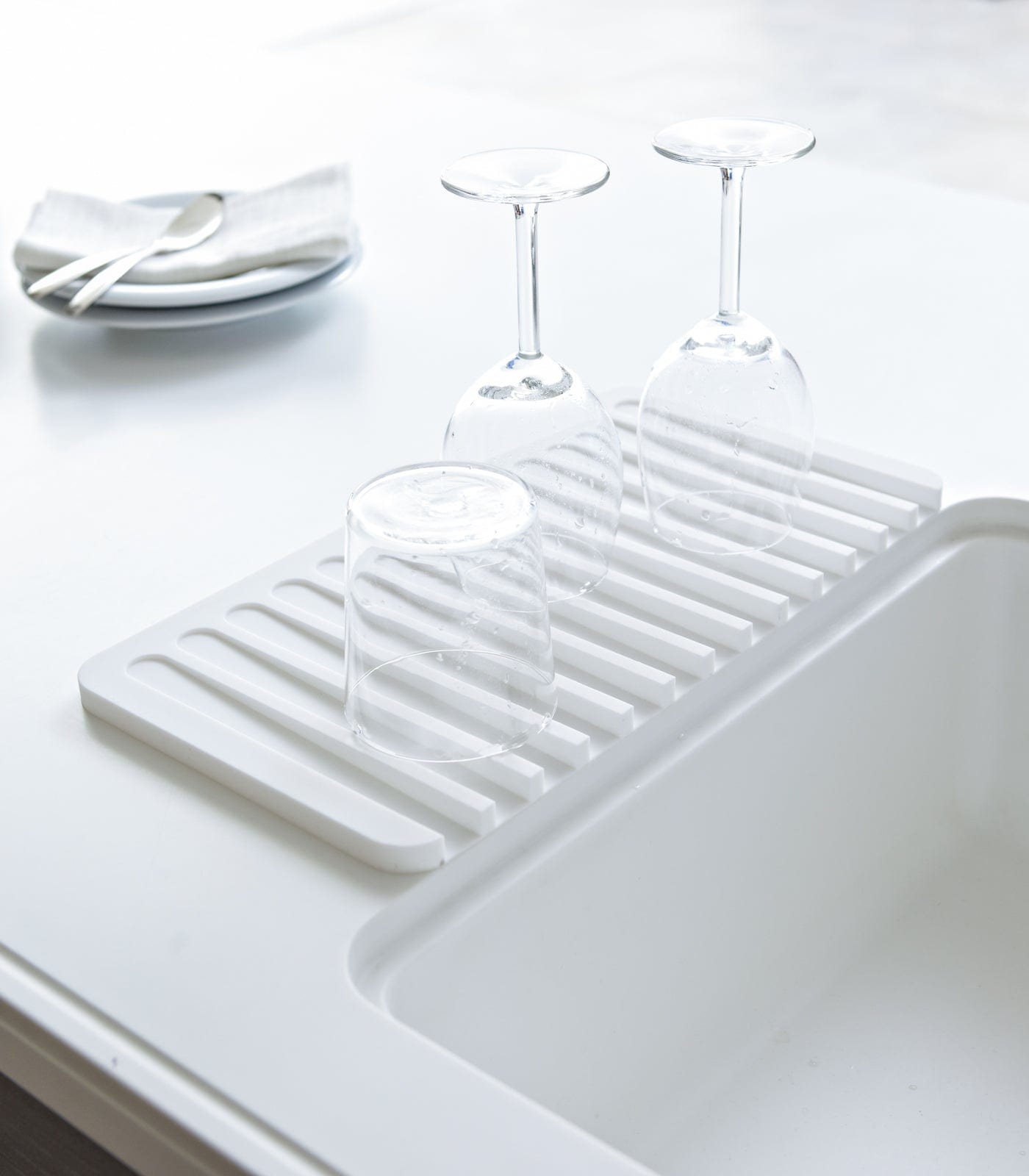White dish rack on a white kitchen counter with glasses and plates.