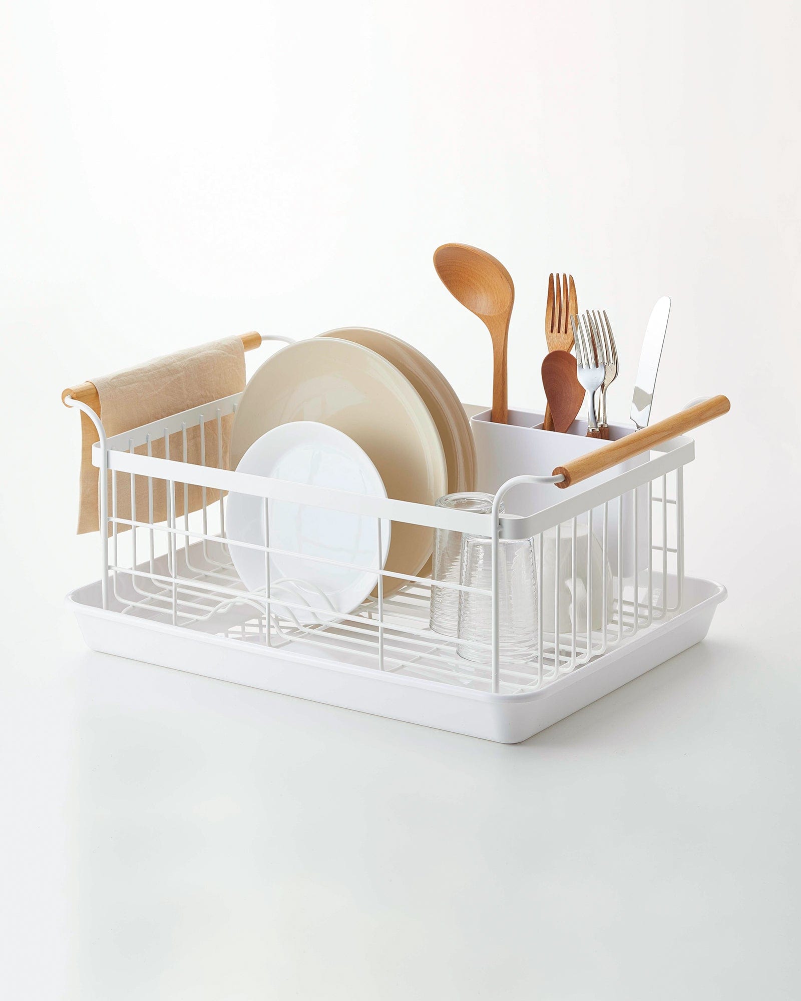 White dish rack with plates, utensils, and a towel on a white background