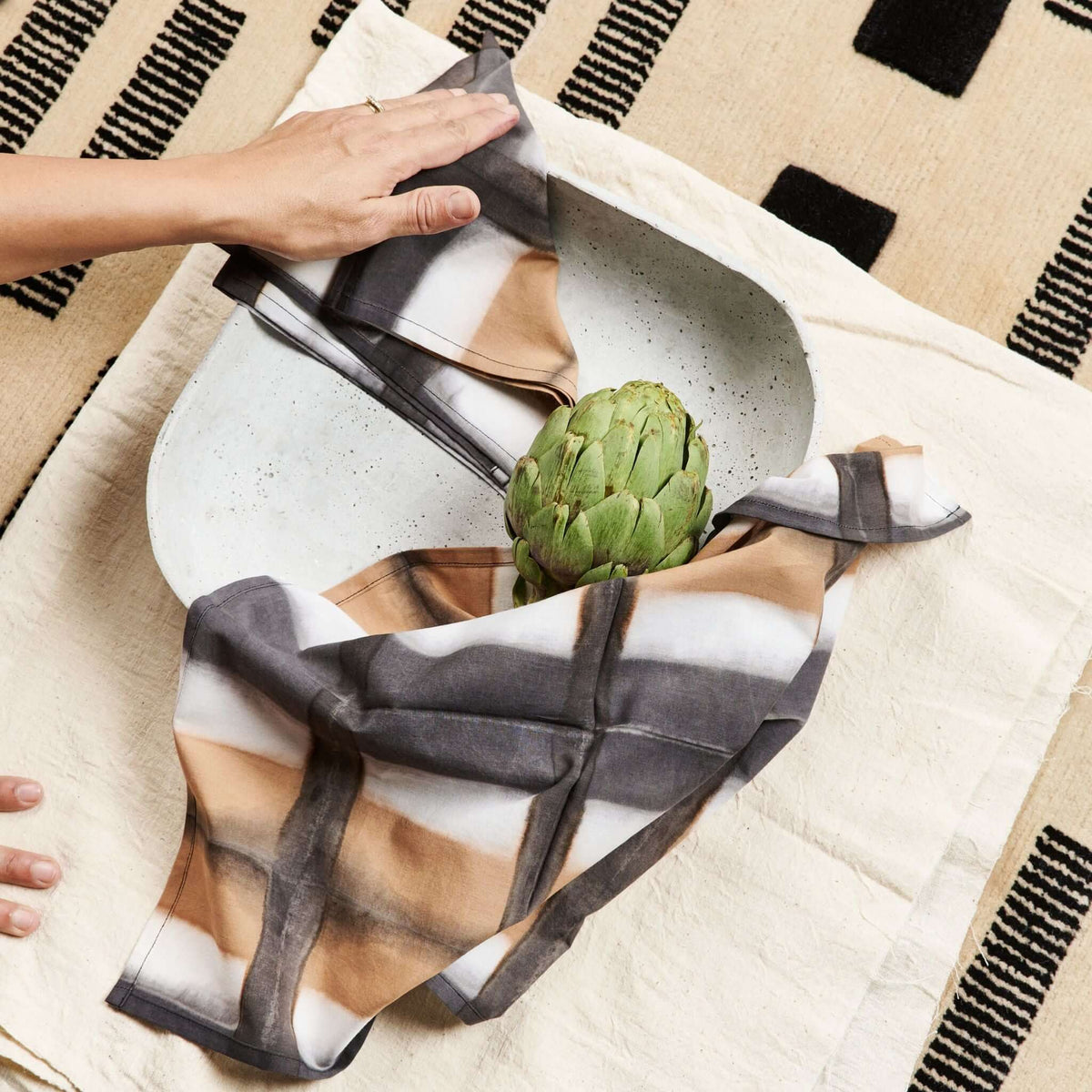 Overhead table setting with Chowk Black napkins arranged around a pale ceramic plate and fresh artichoke