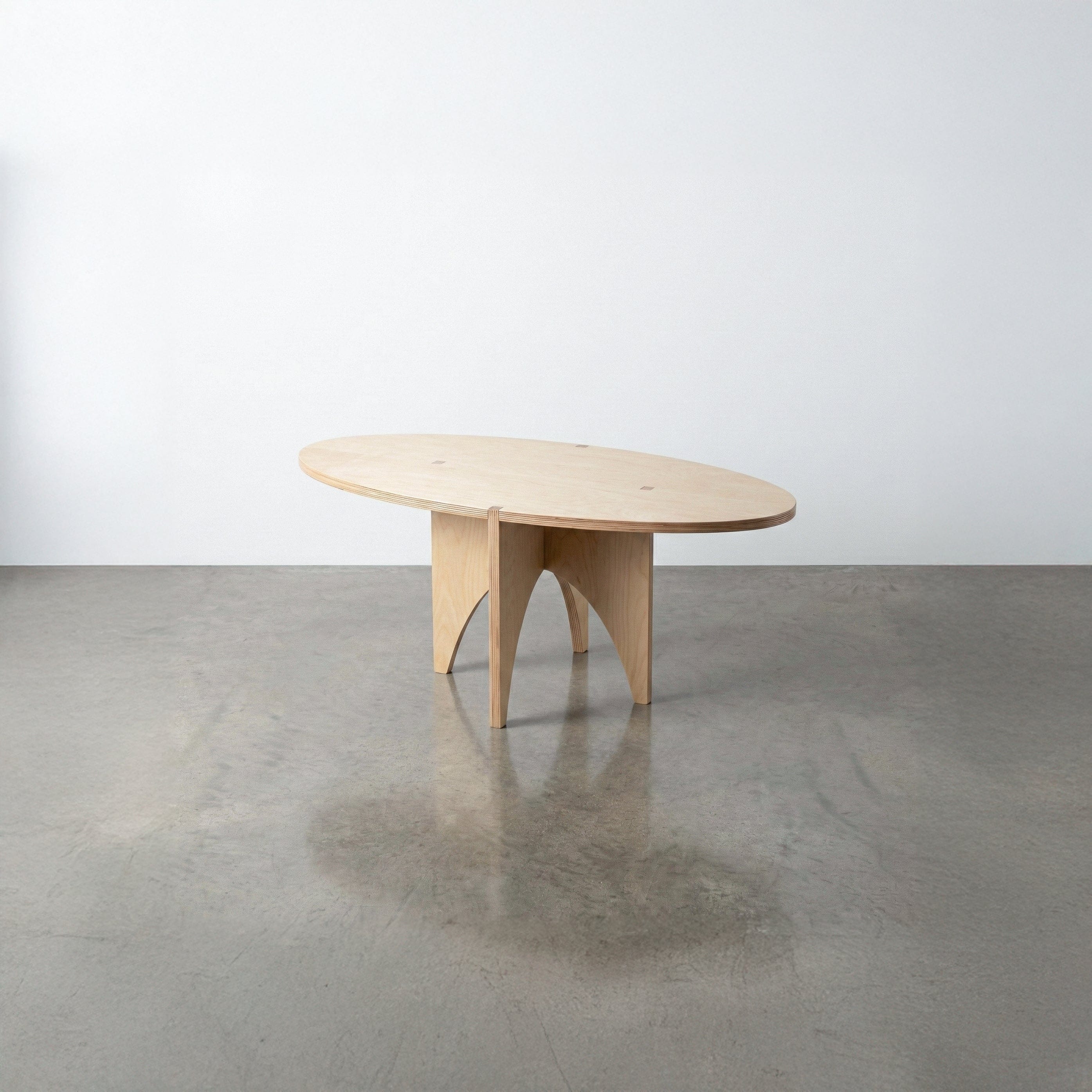 Studio Furnis YOYO natural wood accent table with an elongated oval top and intersecting curved panel legs, displayed on a polished concrete floor